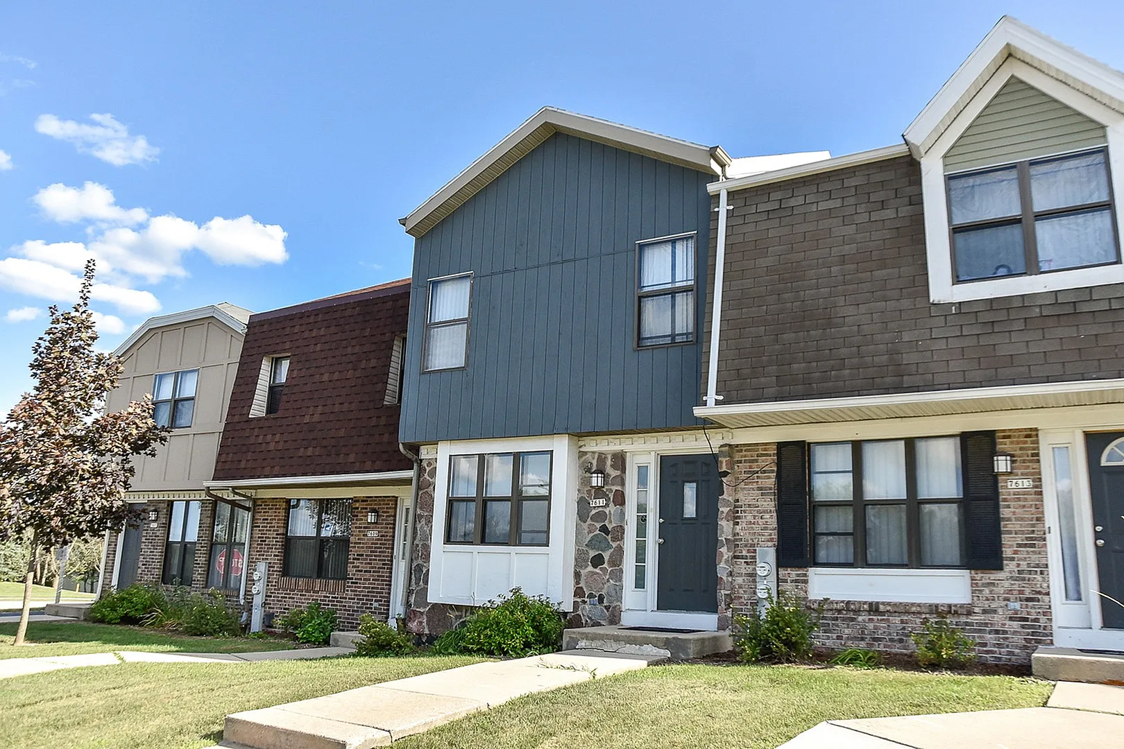 Charming townhouse exterior with diverse architectural styles, featuring brick and wood paneling, nestled under a bright blue sky.
