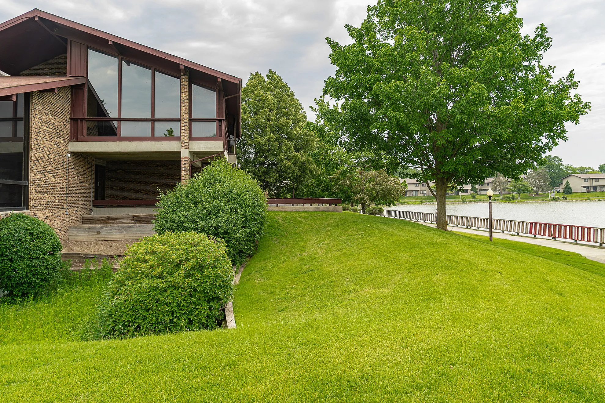Charming lakeside property with lush green lawn, mature trees, and large windows offering stunning waterfront views.