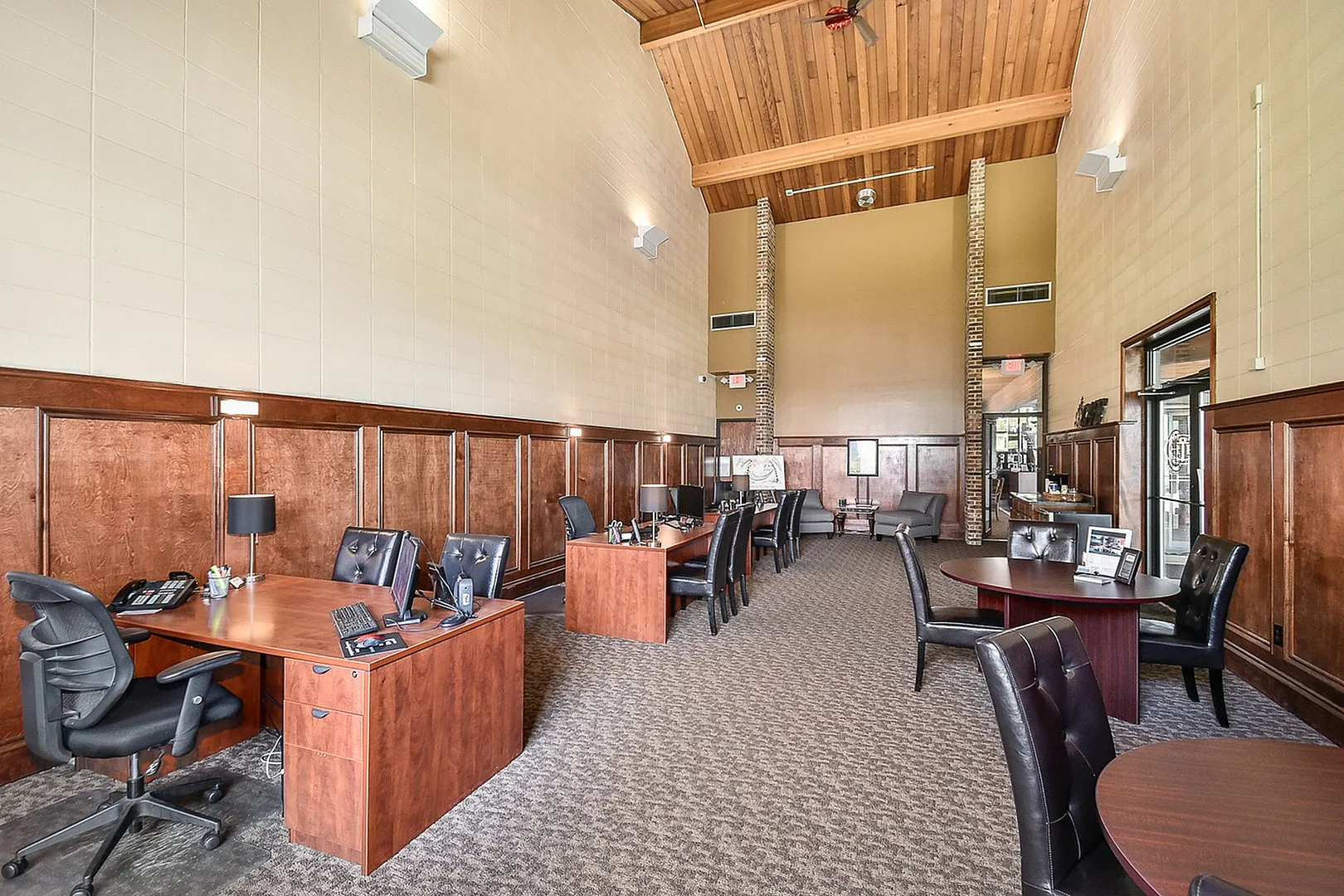 Elegant office space with high wooden ceilings, stylish desks, and plush chairs, perfect for professional meetings.