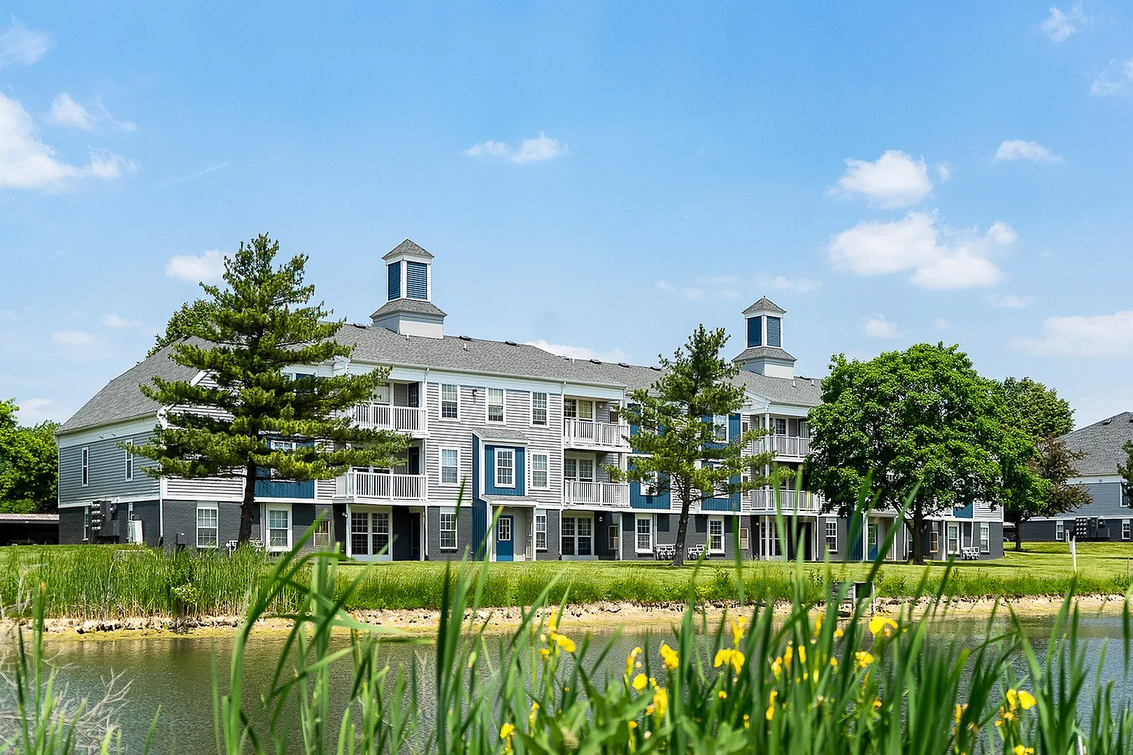 Charming apartment complex surrounded by lush greenery and scenic pond views, offering spacious balconies for relaxation.