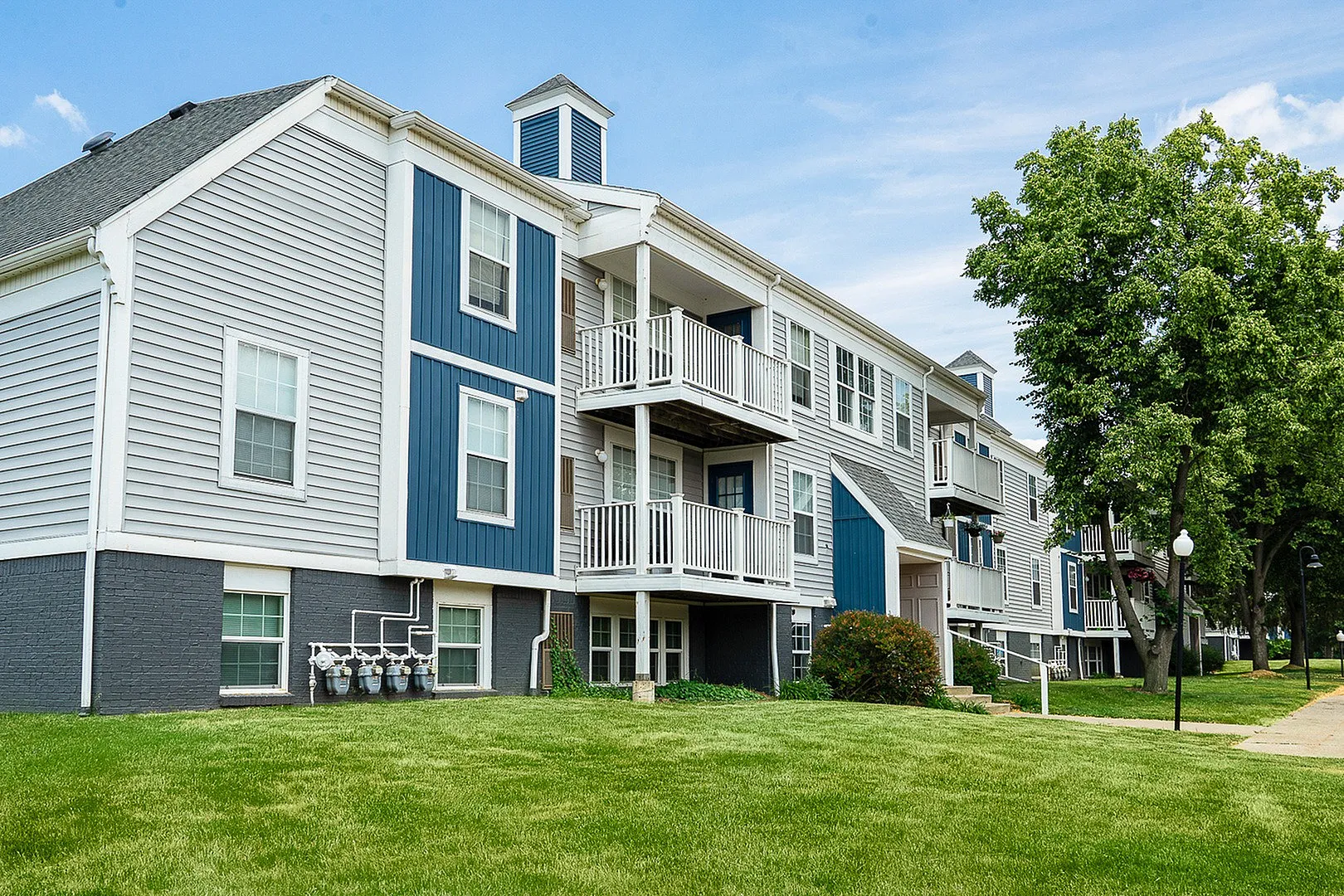 Charming two-story apartment complex with modern balconies, surrounded by lush green lawns and mature trees.