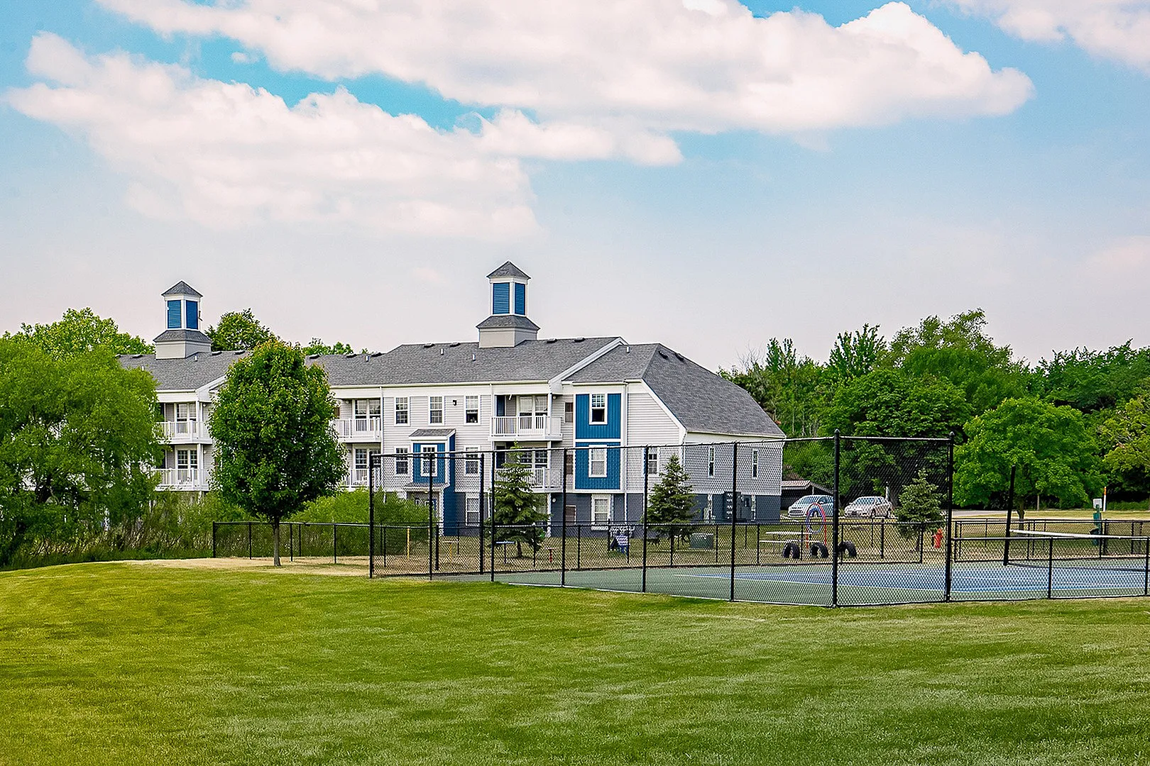 Charming residential building with stylish architecture, surrounded by lush greenery and spacious outdoor tennis court.