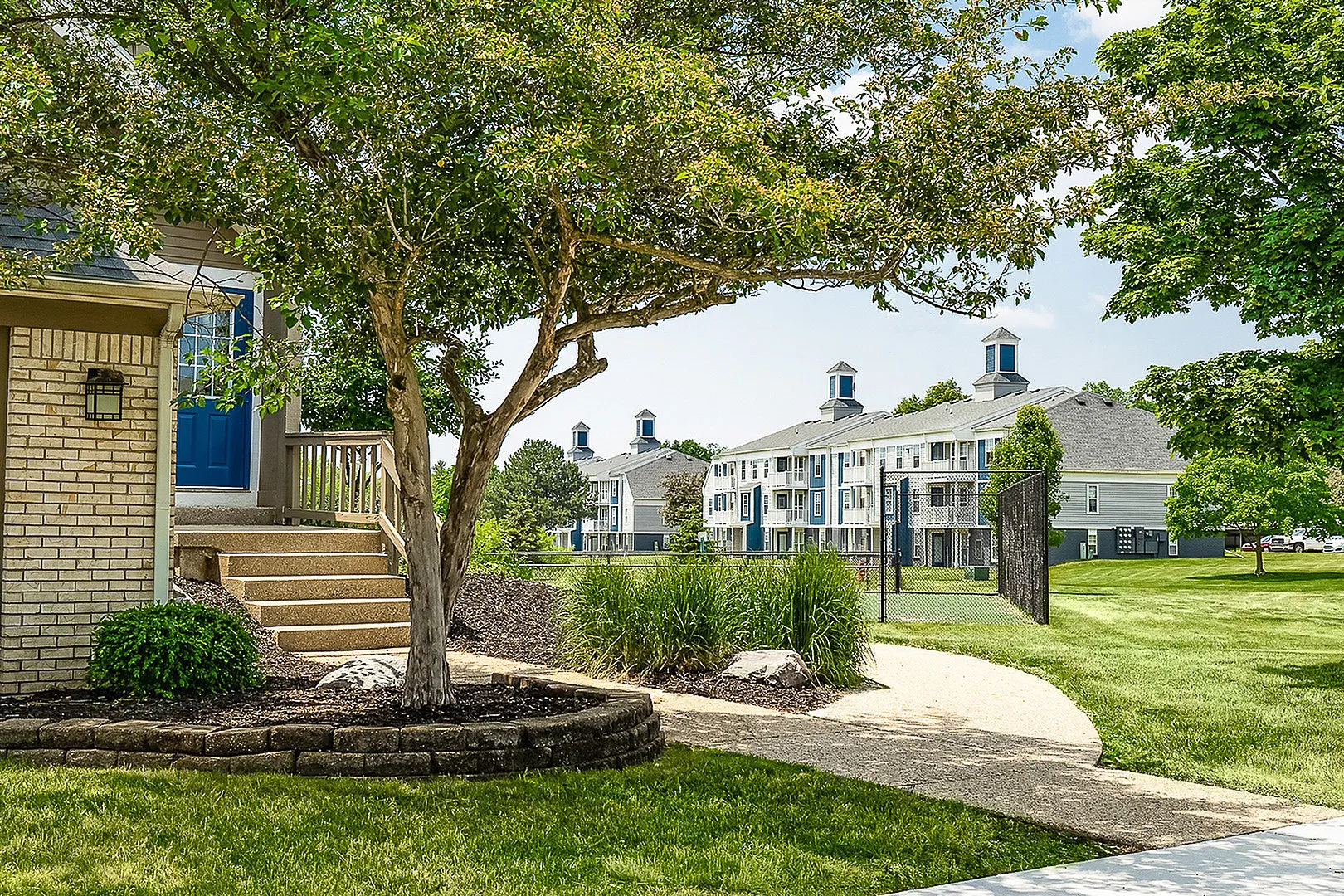 Charming residential complex surrounded by lush greenery, featuring elegant brickwork and vibrant blue accents.