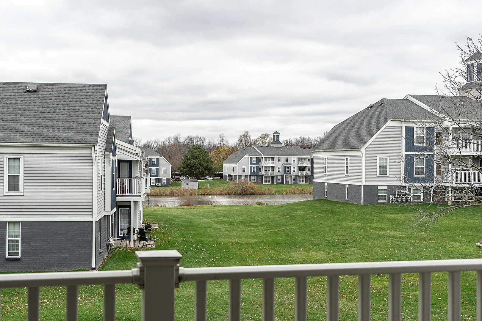 Charming apartment complex with modern architecture, surrounded by lush green lawns and a serene pond view.