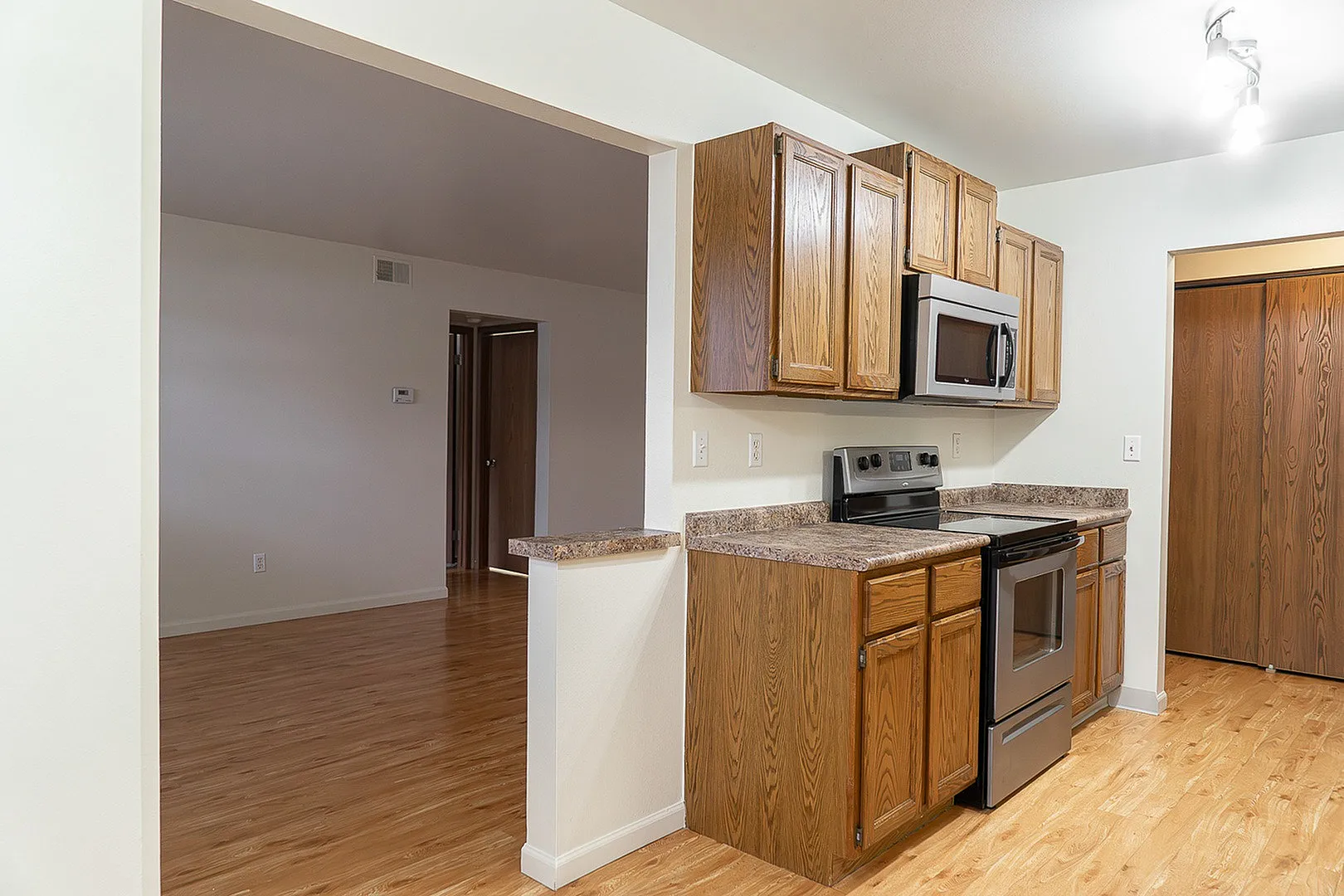Inviting kitchen area with warm wood cabinetry, gleaming modern appliances, and open access to a bright living space featuring elegant hardwood flooring.
