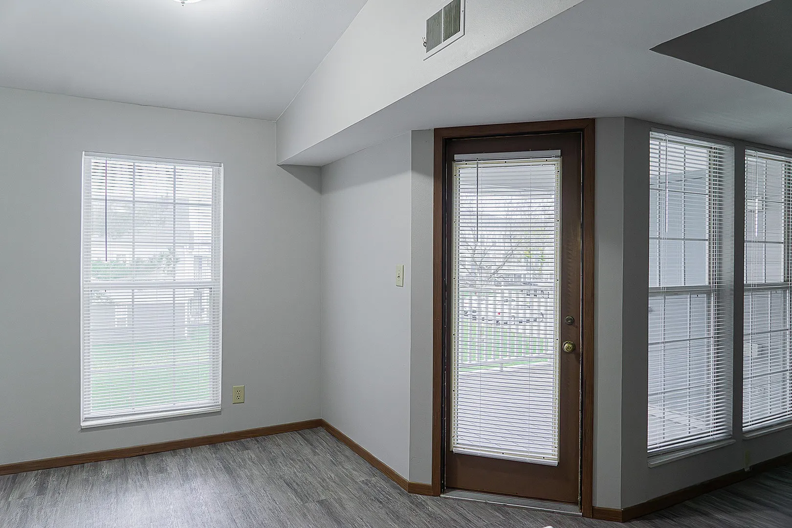 Bright and inviting apartment interior with large windows and sleek wooden flooring, leading to a charming outdoor view.