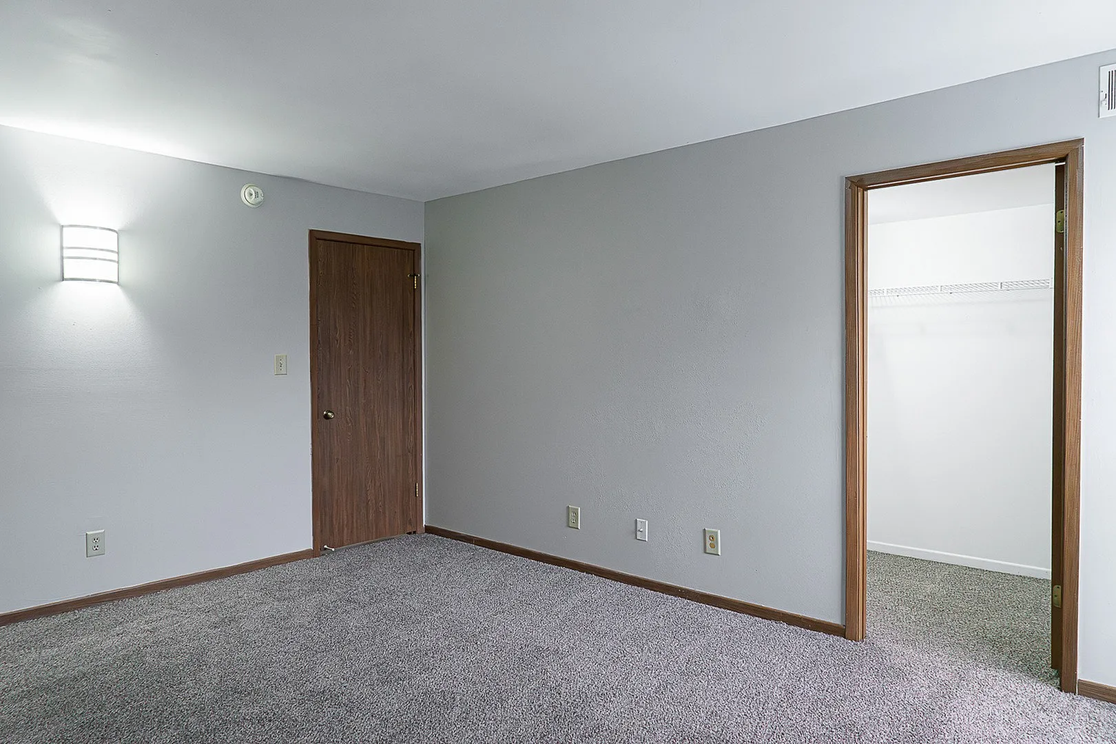 Spacious bedroom with plush carpet, modern wall light, and a walk-in closet, offering a serene and cozy living space.