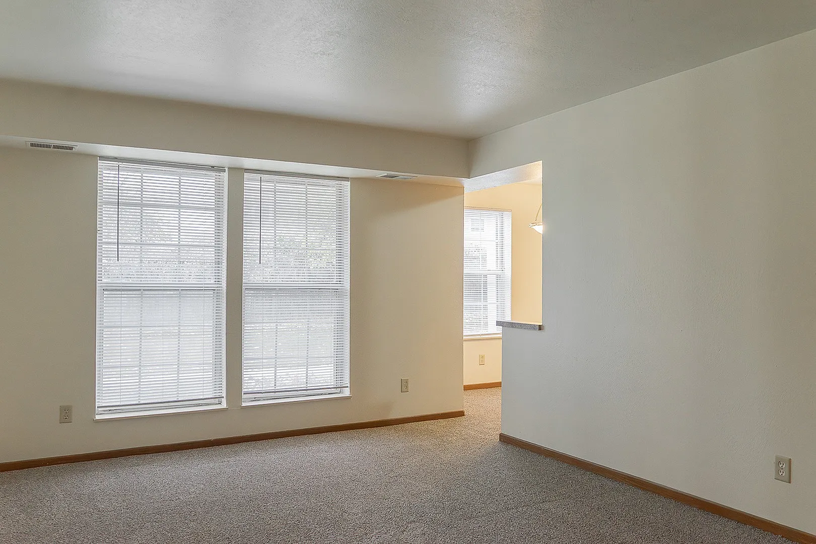 Bright living space with large windows and neutral tones, connecting to a cozy kitchen nook.
