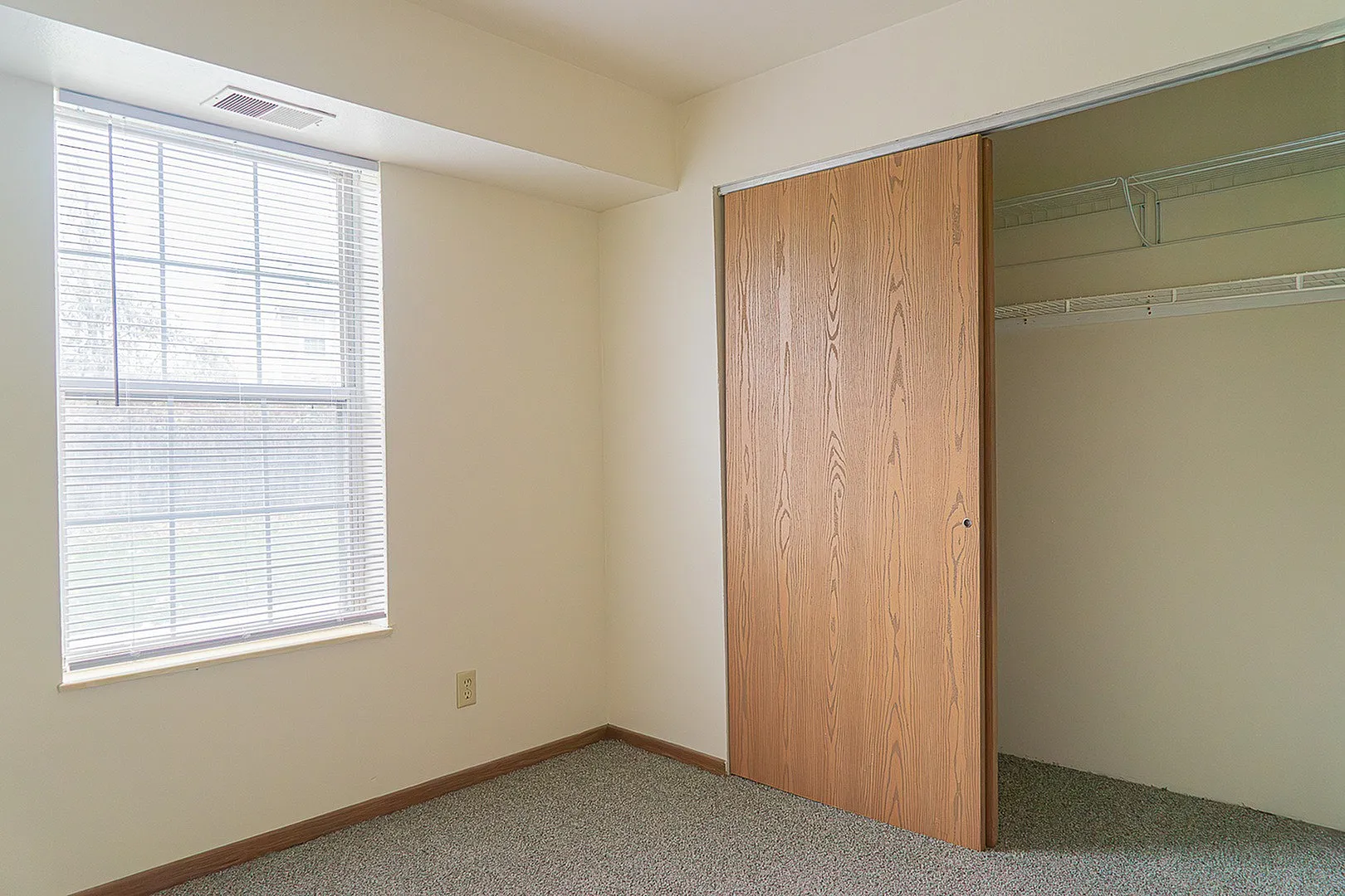 Bright bedroom with large window, natural light, and spacious closet with wooden sliding doors.