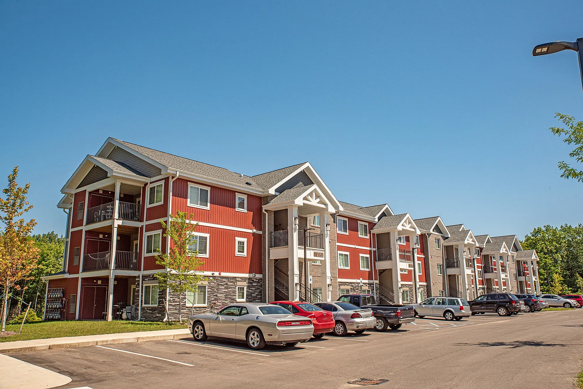 Charming, modern apartment complex with red and beige exterior, featuring spacious balconies and a lush green surrounding.