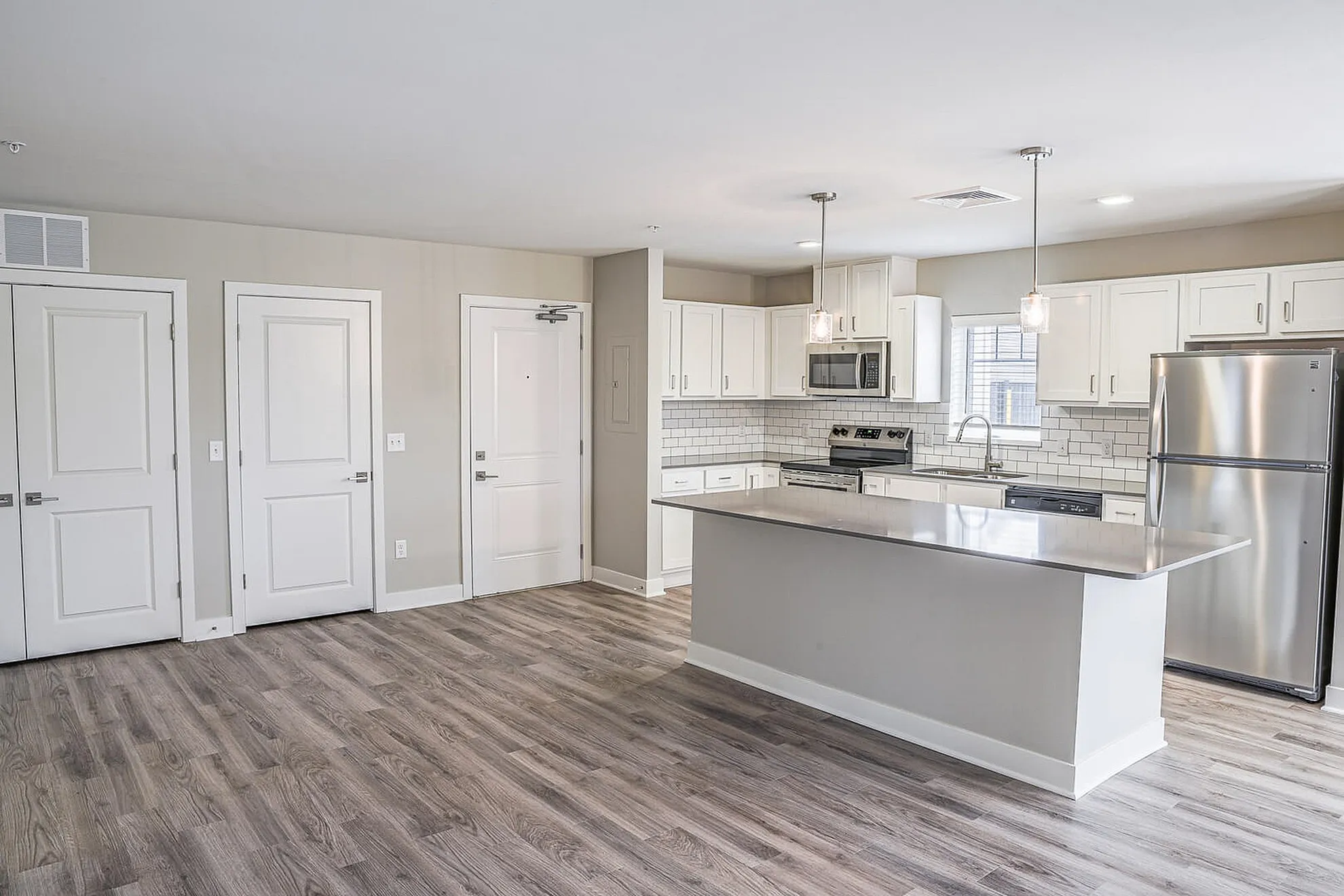 Modern open-plan kitchen with sleek stainless steel appliances and a stylish island, featuring bright pendant lighting and elegant wood flooring.