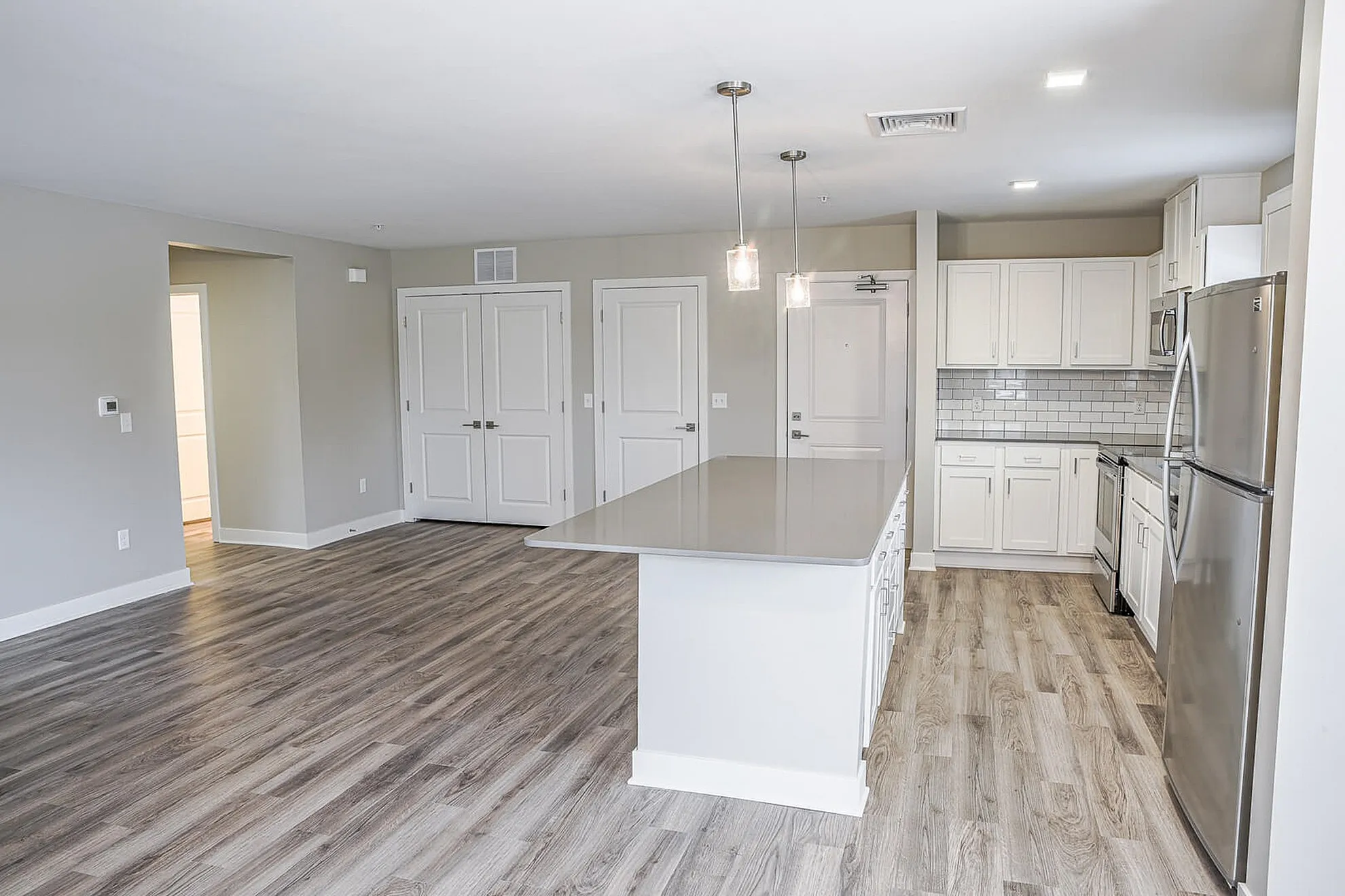 Modern open-concept kitchen and living area with elegant wood flooring, sleek white cabinetry, and stainless steel appliances.