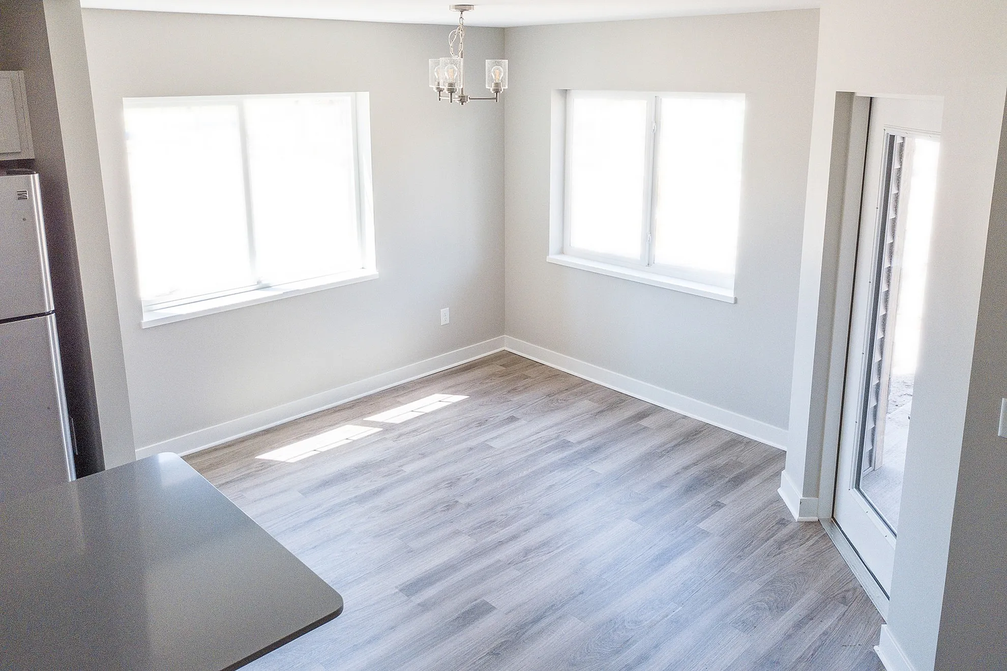 Bright and airy room with large windows, modern laminate flooring, and a chic ceiling light, perfect for a dining area or office space.