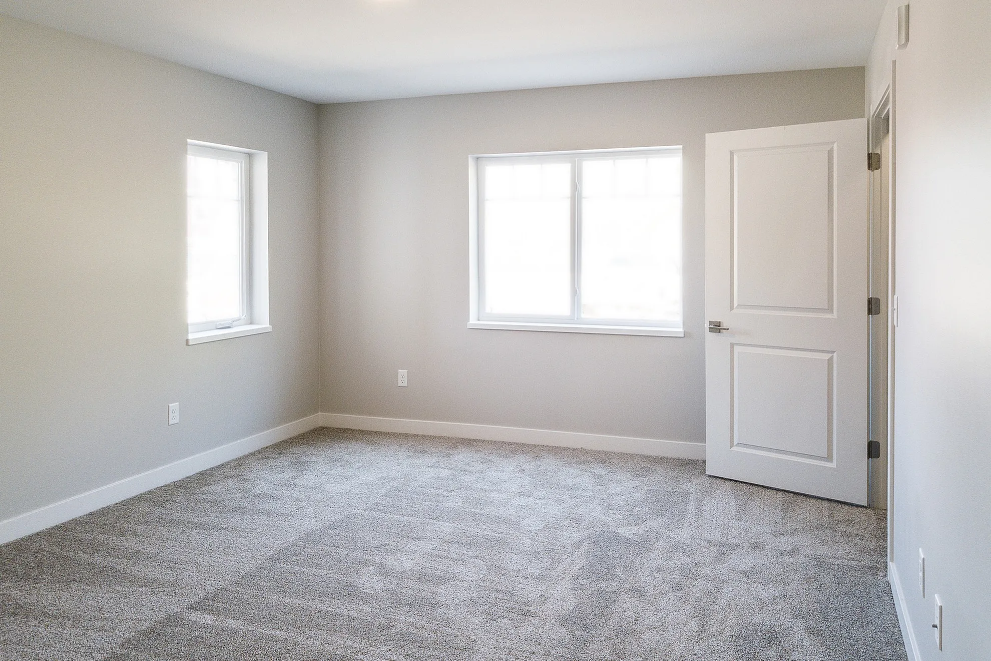 Bright and spacious bedroom with large windows, soft carpeting, and neutral wall tones.