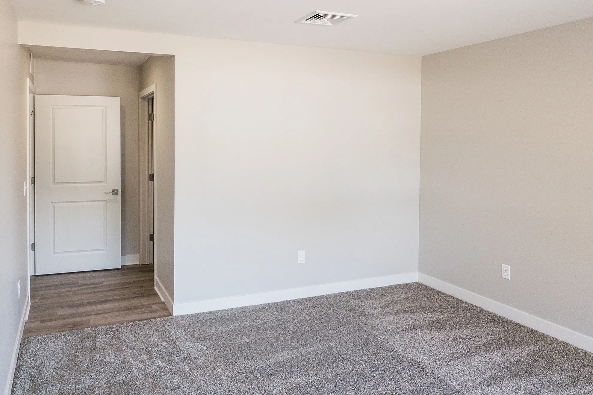 Bright and spacious room featuring plush carpeting, pristine white walls, and elegant wood flooring at the entrance.