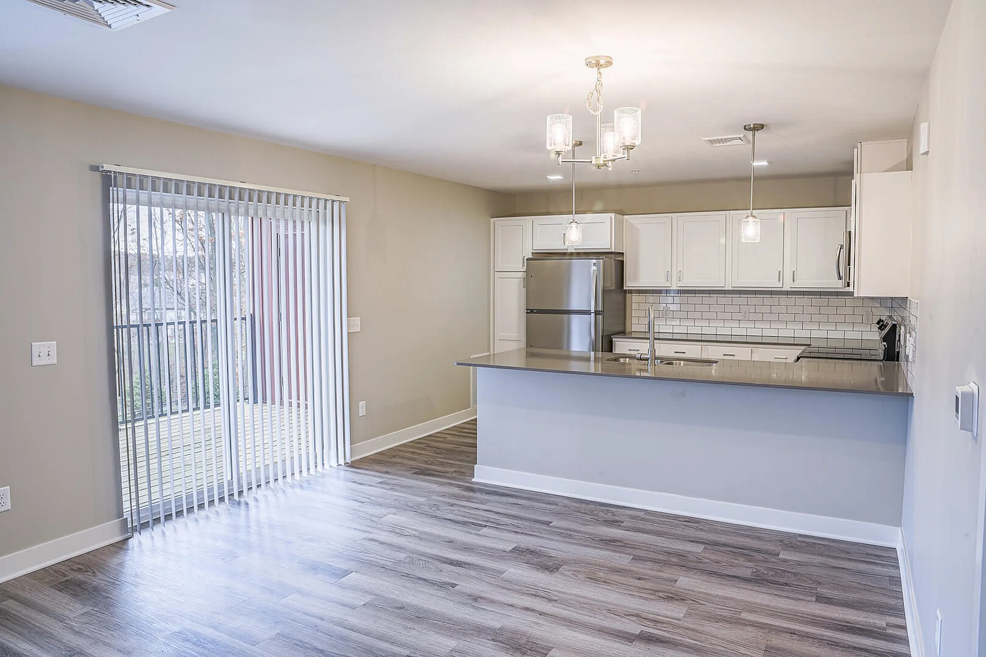 Bright open-concept kitchen with modern stainless steel appliances, sleek countertops, and elegant pendant lighting overlooking a spacious living area with large sliding glass doors.