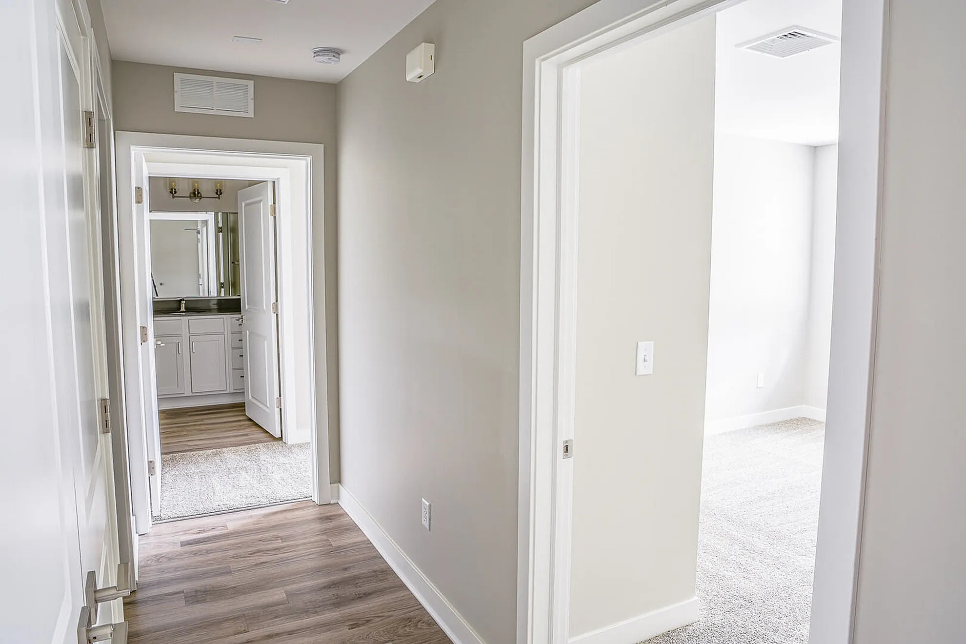 Bright, modern hallway with wooden flooring leading to a stylish bathroom with elegant cabinetry.