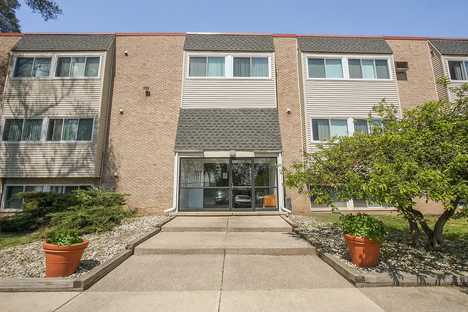 Charming apartment building entrance with modern brick facade, elegant landscaping, and inviting pathway.