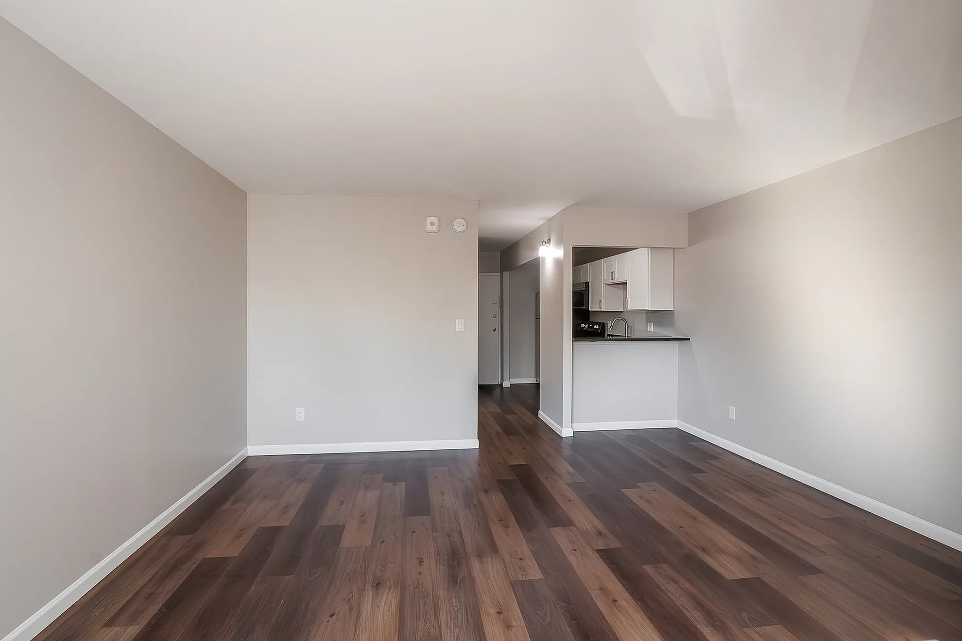Modern living space with elegant hardwood flooring and a cozy kitchen area, perfect for open-concept design enthusiasts.