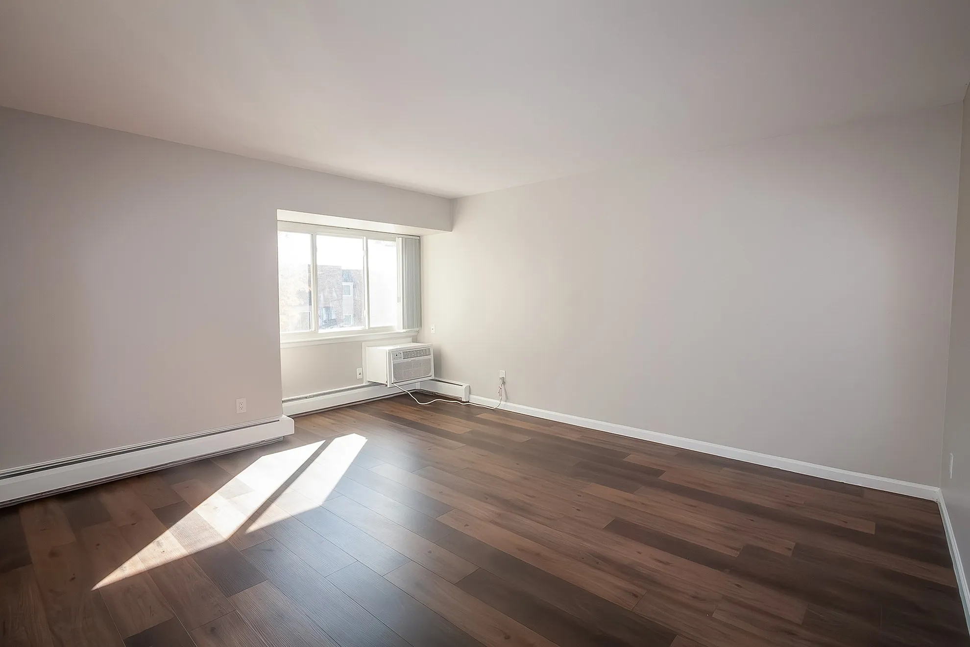 Bright and spacious living room with elegant hardwood floors and a large window, perfect for natural light and modern comfort.