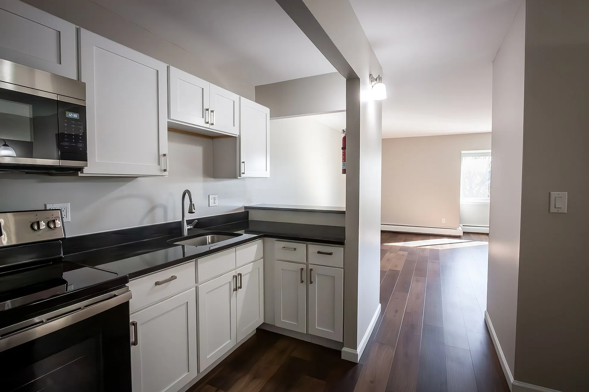 Modern kitchen with sleek white cabinetry and black countertops leading to a sunlit living area with polished hardwood floors.