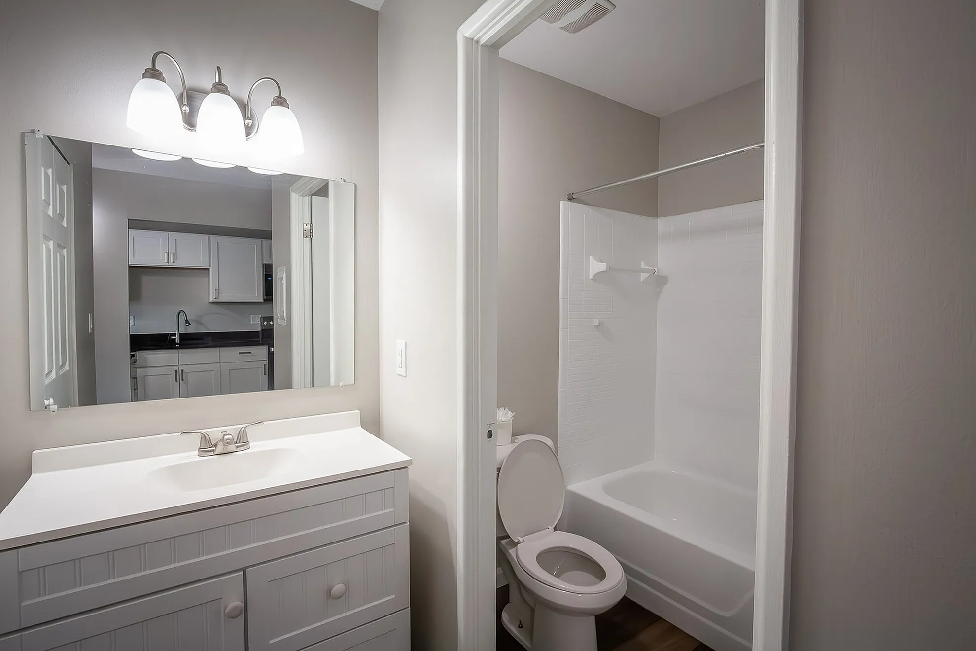 Bright and modern bathroom with sleek vanity and large mirror, adjacent to a pristine kitchen glimpse, offering functional elegance.