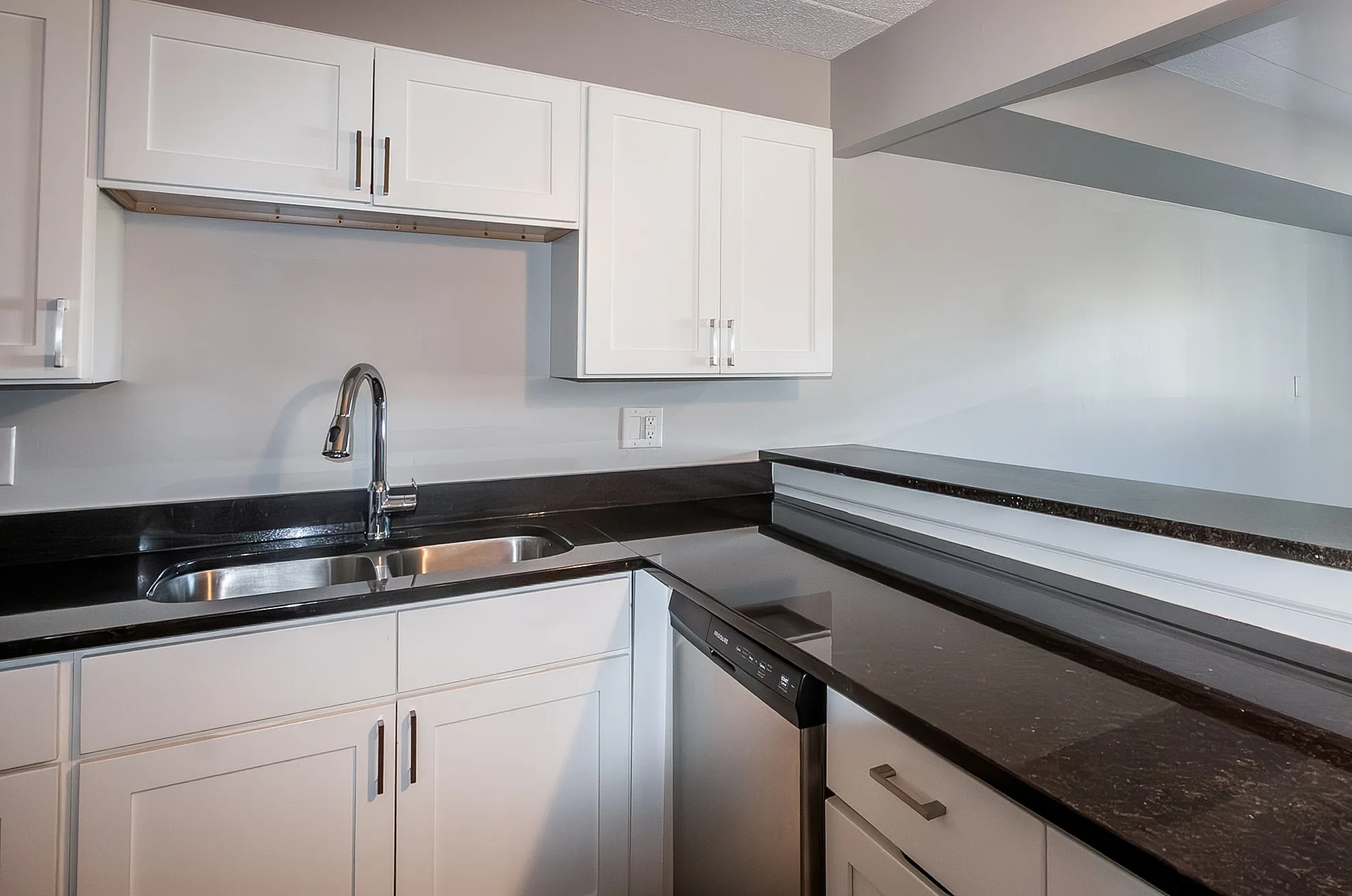 Modern kitchen with sleek black countertops, stainless steel sink, and elegant white cabinetry.