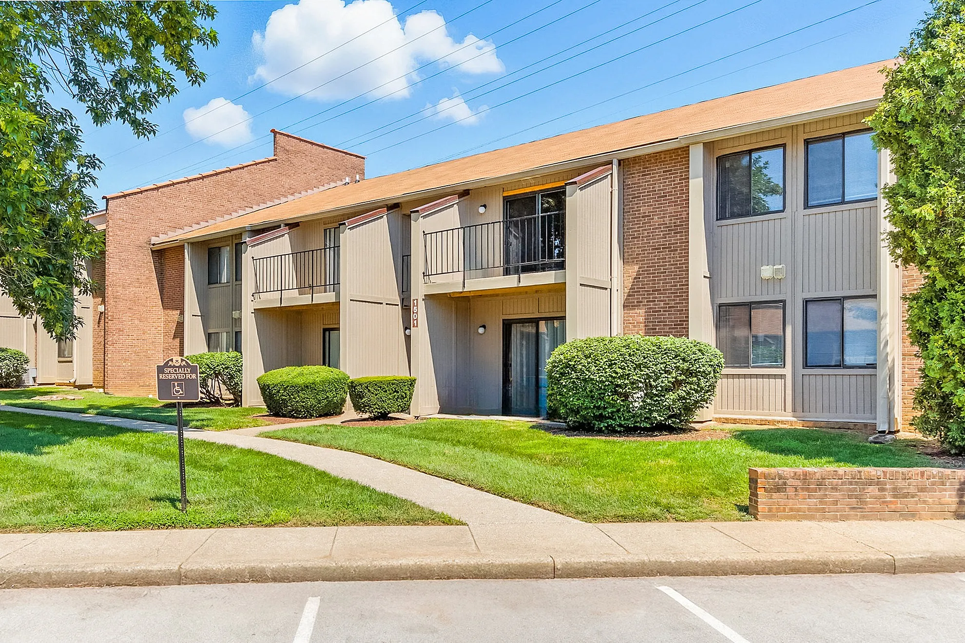 Inviting modern apartment complex with attractive brick and siding design, featuring cozy private balconies and lush green landscaping under a vibrant blue sky.