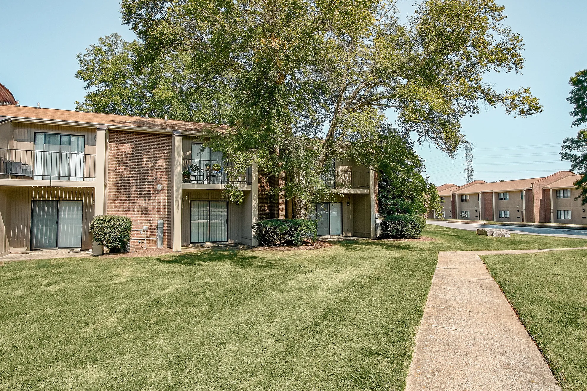 Charming two-story apartment building with balconies surrounded by lush greenery and well-maintained landscaping.