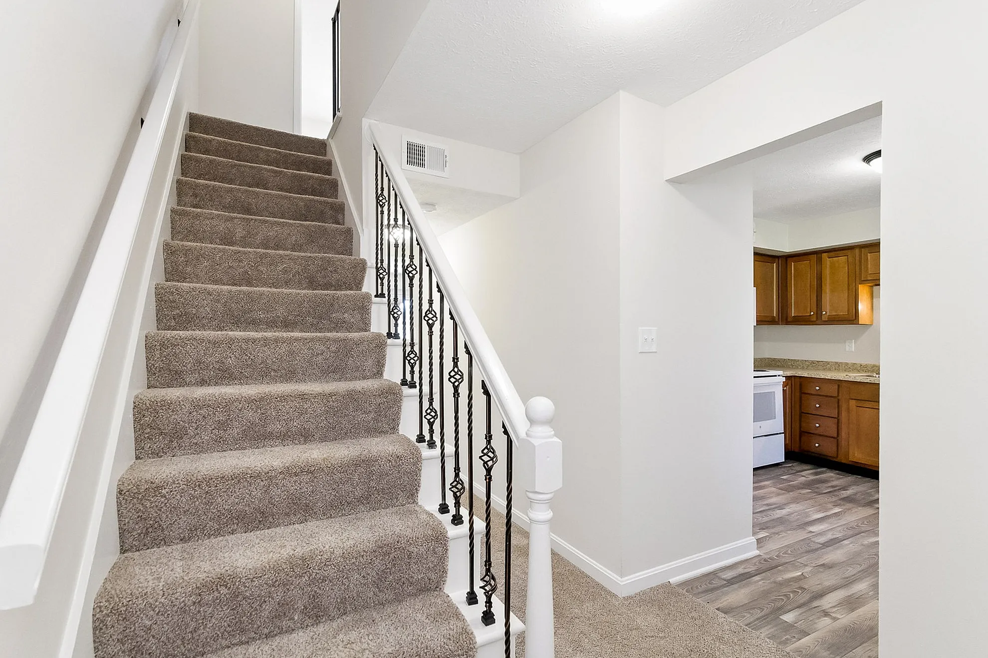 Charming interior with carpeted staircase and open view into the modern kitchen featuring warm wood cabinetry.