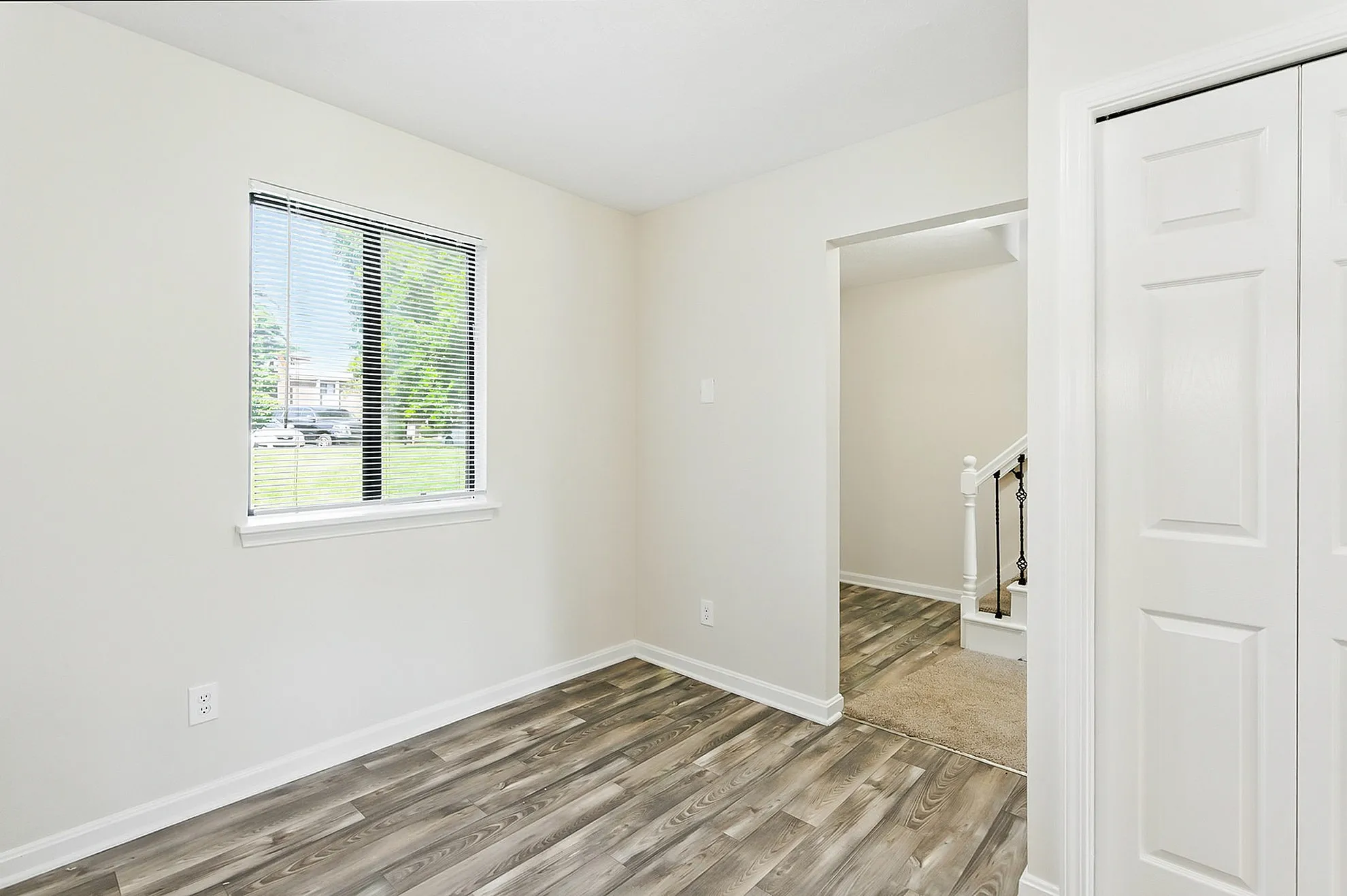 Bright and airy room featuring sleek laminate flooring, large window overlooking lush greenery, and a modern, minimalist design.