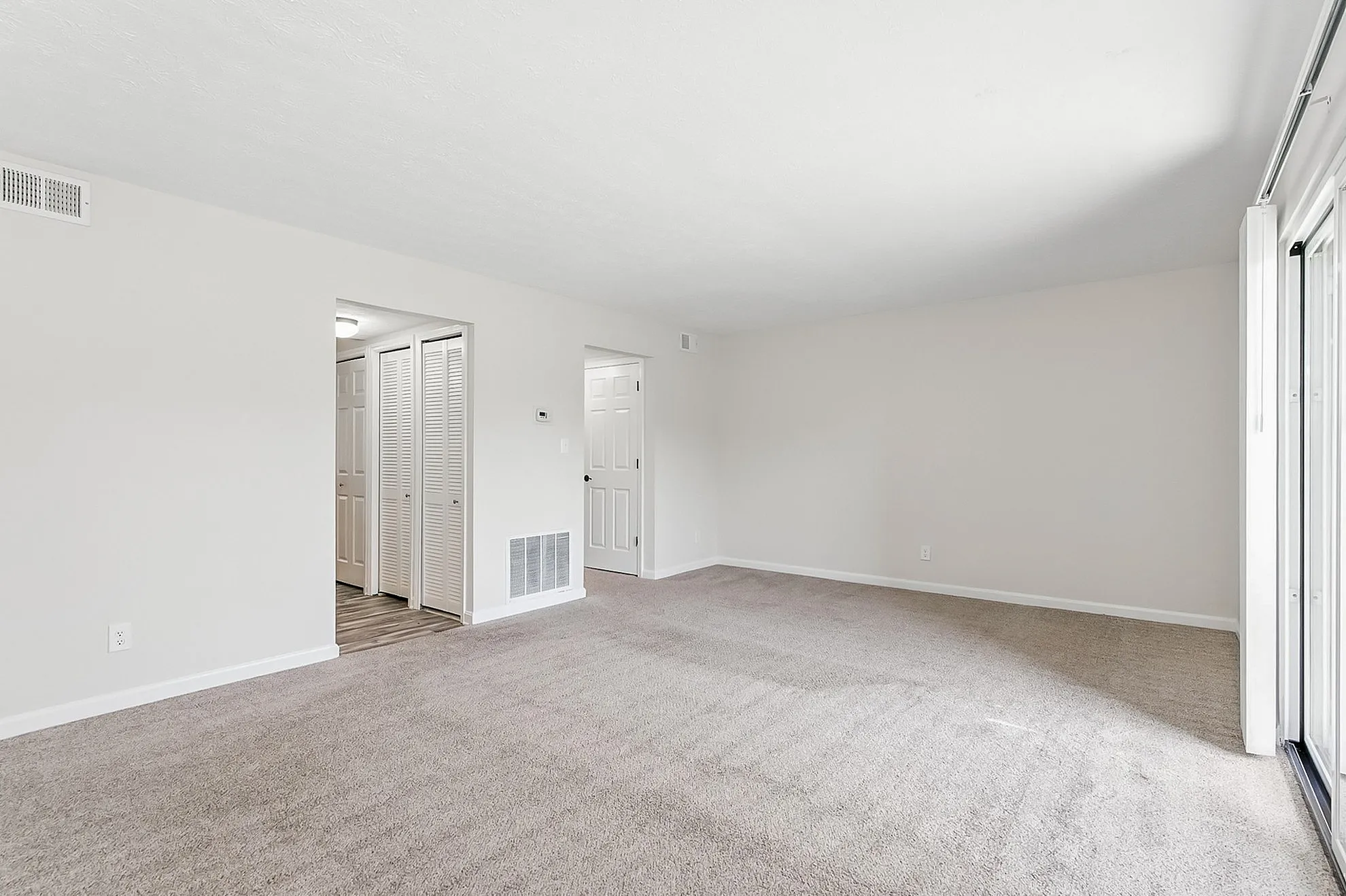 Bright and spacious living area with plush carpet and elegant neutral tones, featuring sliding glass doors for natural light.