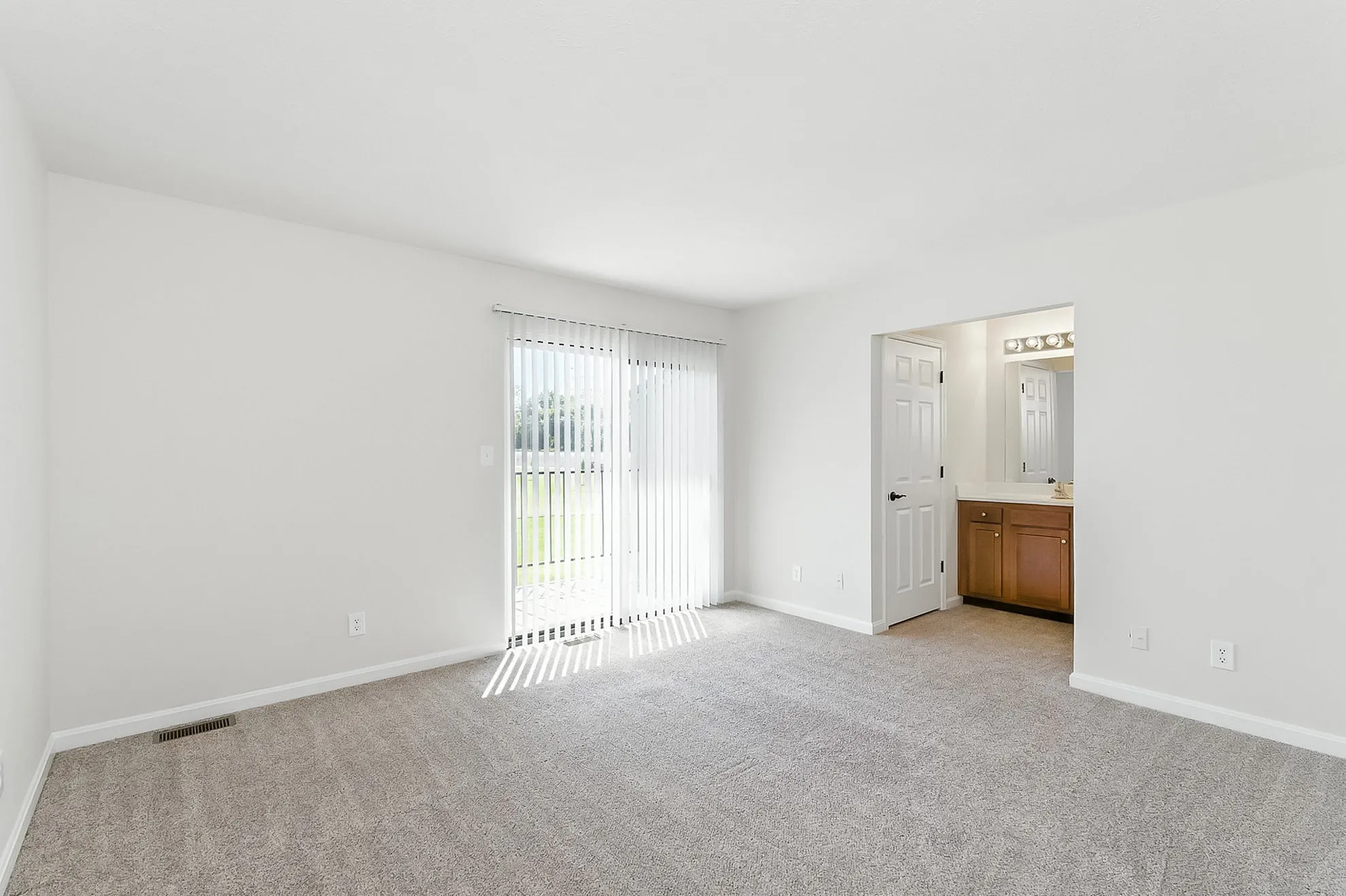 Bright, spacious living area with plush carpet, sliding glass doors, and a glimpse of a modern bathroom, offering a welcoming home ambiance.