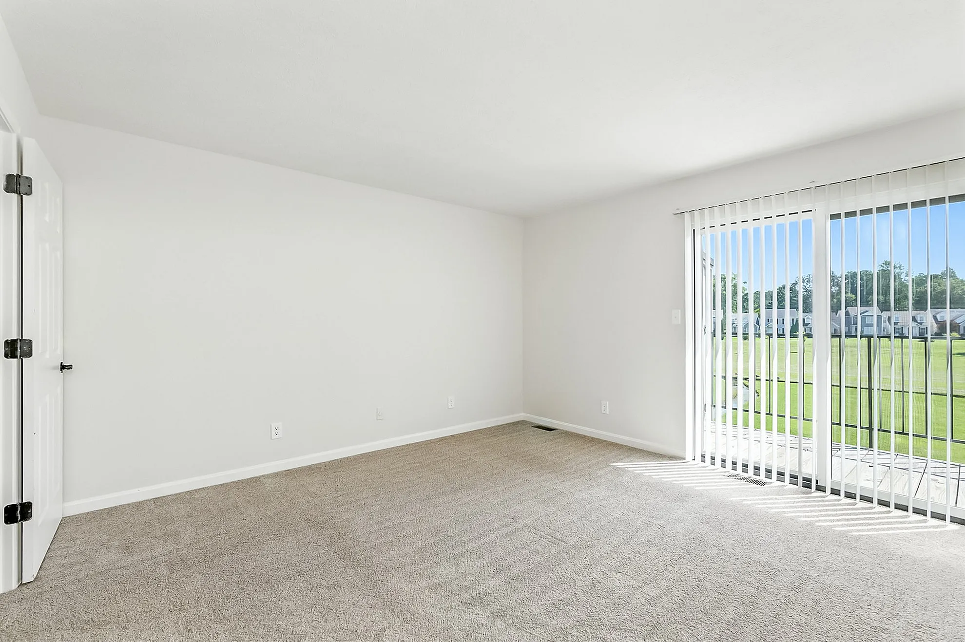 Bright and airy room with plush carpet and sliding glass doors leading to a serene outdoor view.