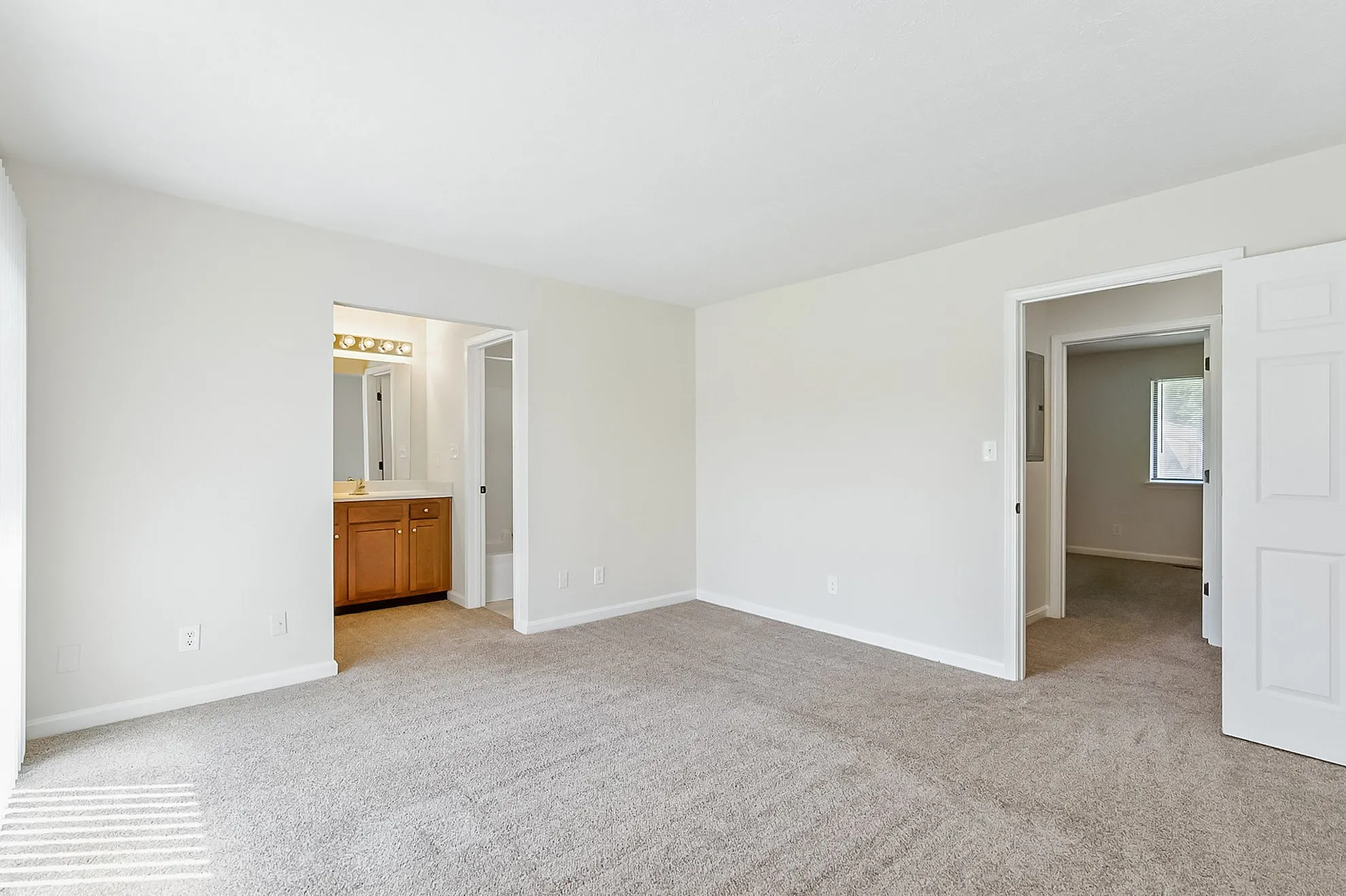 Bright and spacious bedroom with plush carpet, featuring a view into an ensuite bathroom with elegant wooden cabinetry.