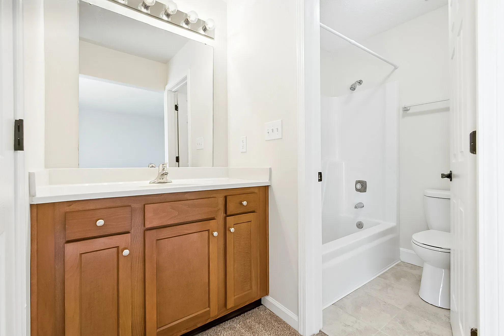 Bright and inviting bathroom featuring elegant wood cabinetry, a large mirror, and a pristine bathtub setup.