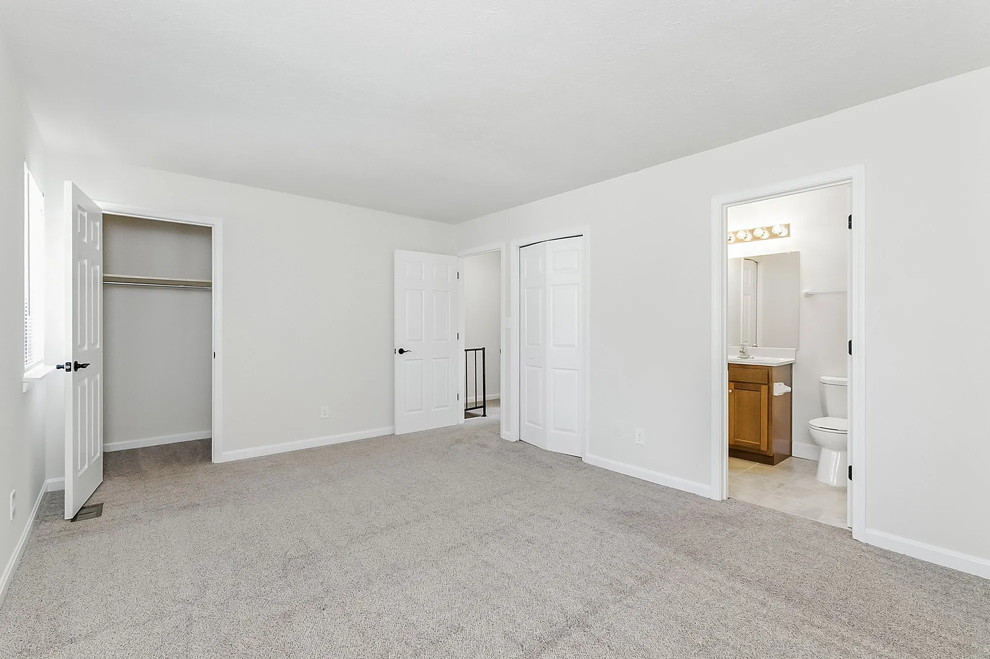 Bright and spacious bedroom with soft carpeting, open closet, and ensuite bathroom for modern living.