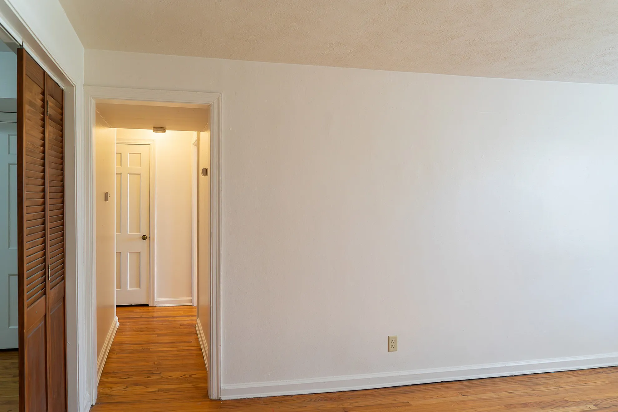 Bright and inviting hallway with elegant wood flooring and pristine white walls, leading to multiple rooms.
