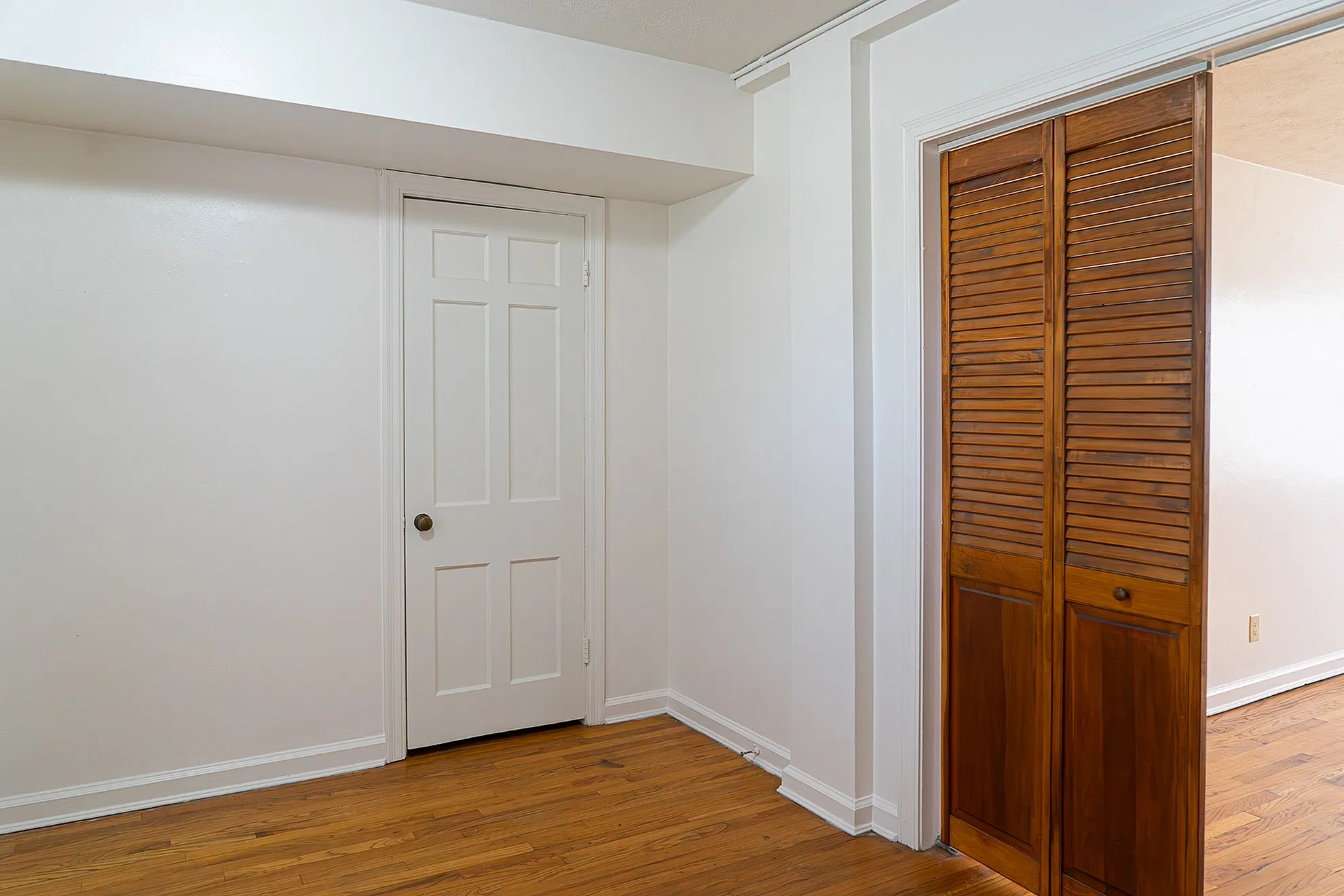 Elegant interior corner with pristine white walls and warm wooden floors, featuring classic white and rich wooden doors.
