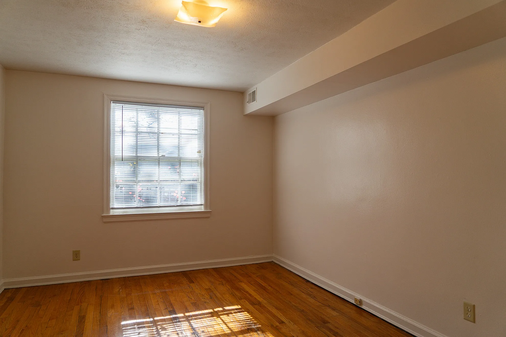 Bright and inviting room with polished hardwood floors and a large window offering ample natural light.