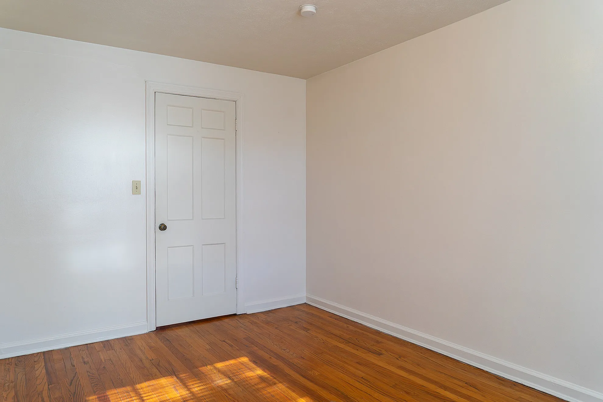 Bright and pristine room with elegant hardwood floors and a classic white door, perfect for a serene living space.