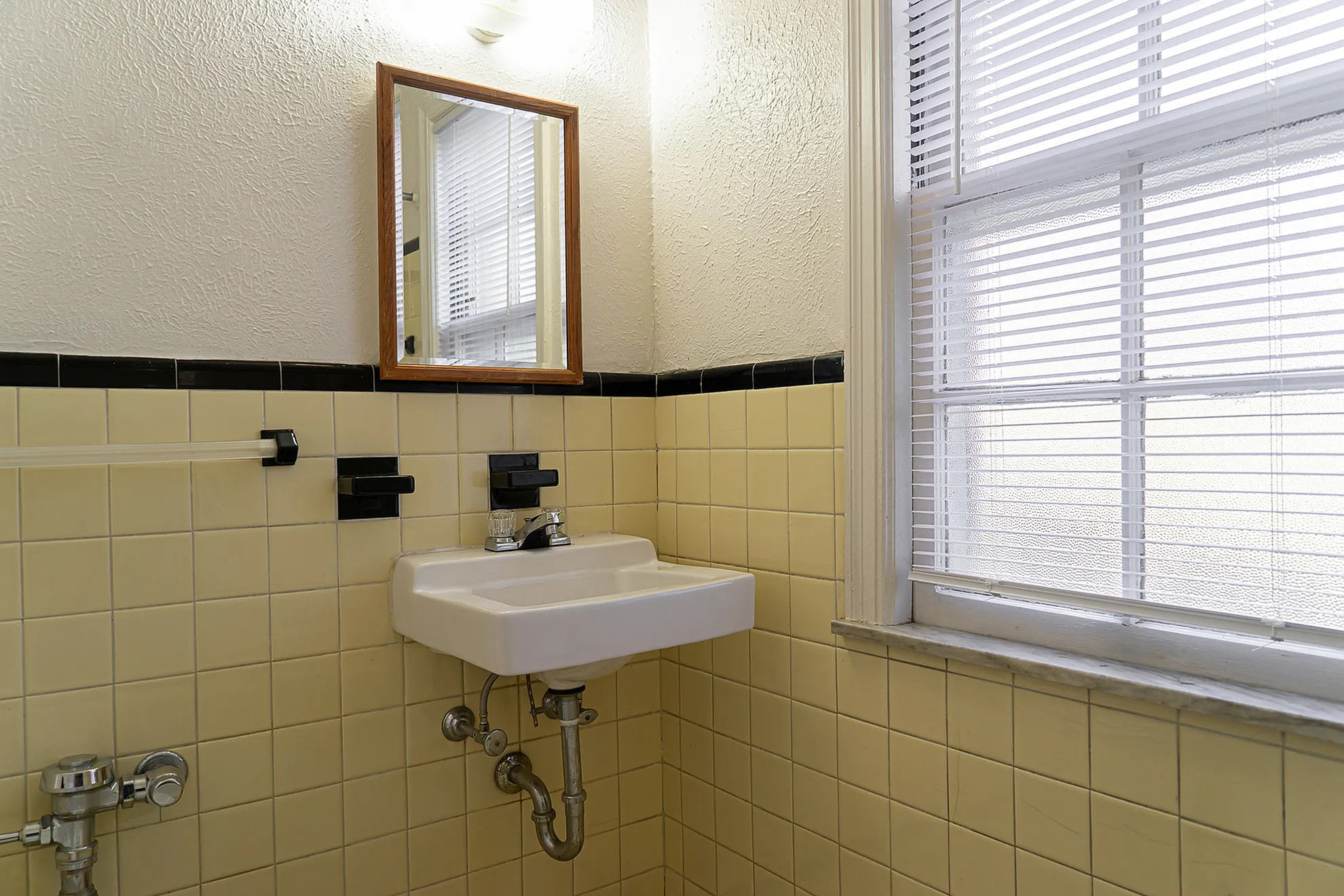 Charming bathroom corner with retro yellow tiles, a classic sink, and large window for natural light.