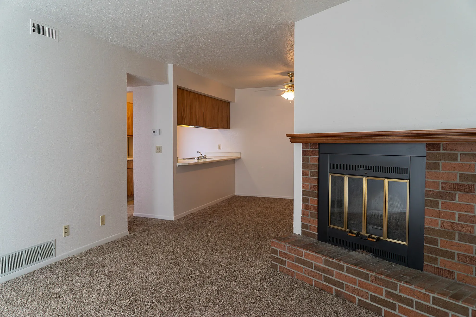 Cozy living area featuring a charming brick fireplace, plush carpeting, and a stylish open kitchen design.