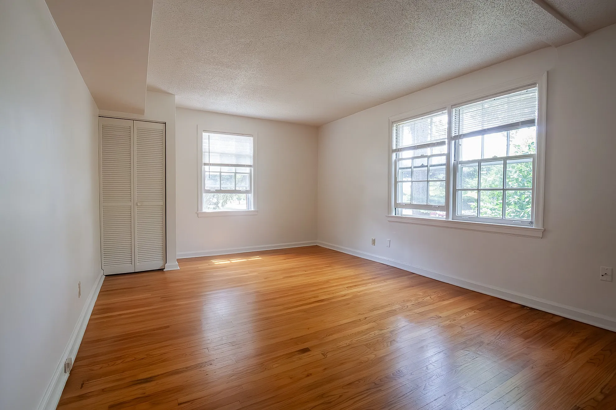 Bright and spacious room with beautiful hardwood flooring and ample natural light from large windows.