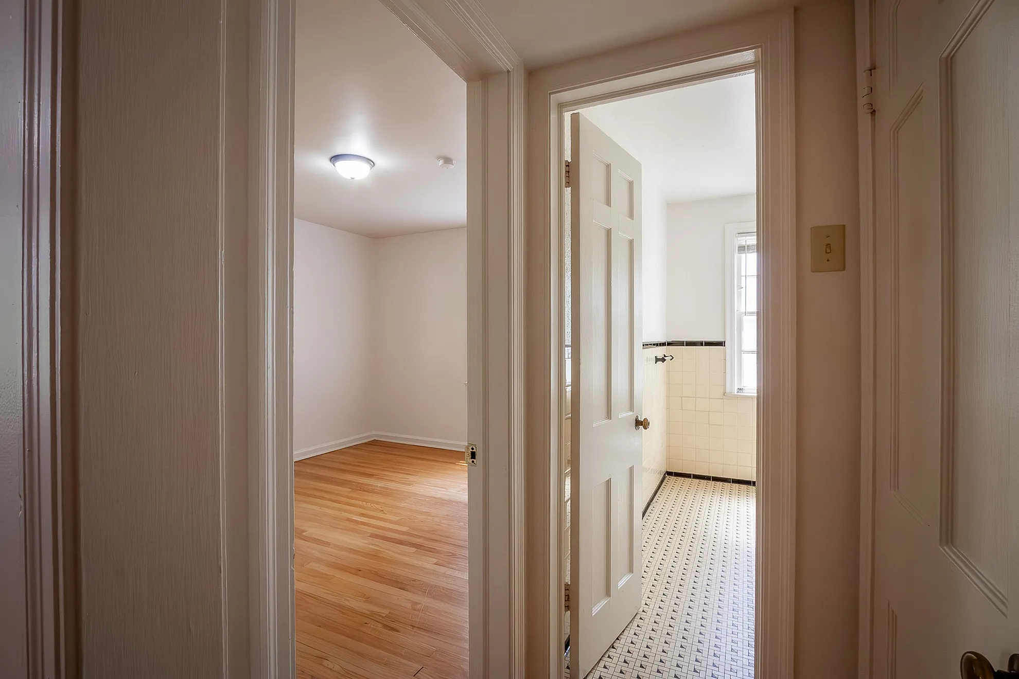 Inviting apartment hallway leads to a sunlit room with elegant hardwood floors and a classic tiled bathroom.