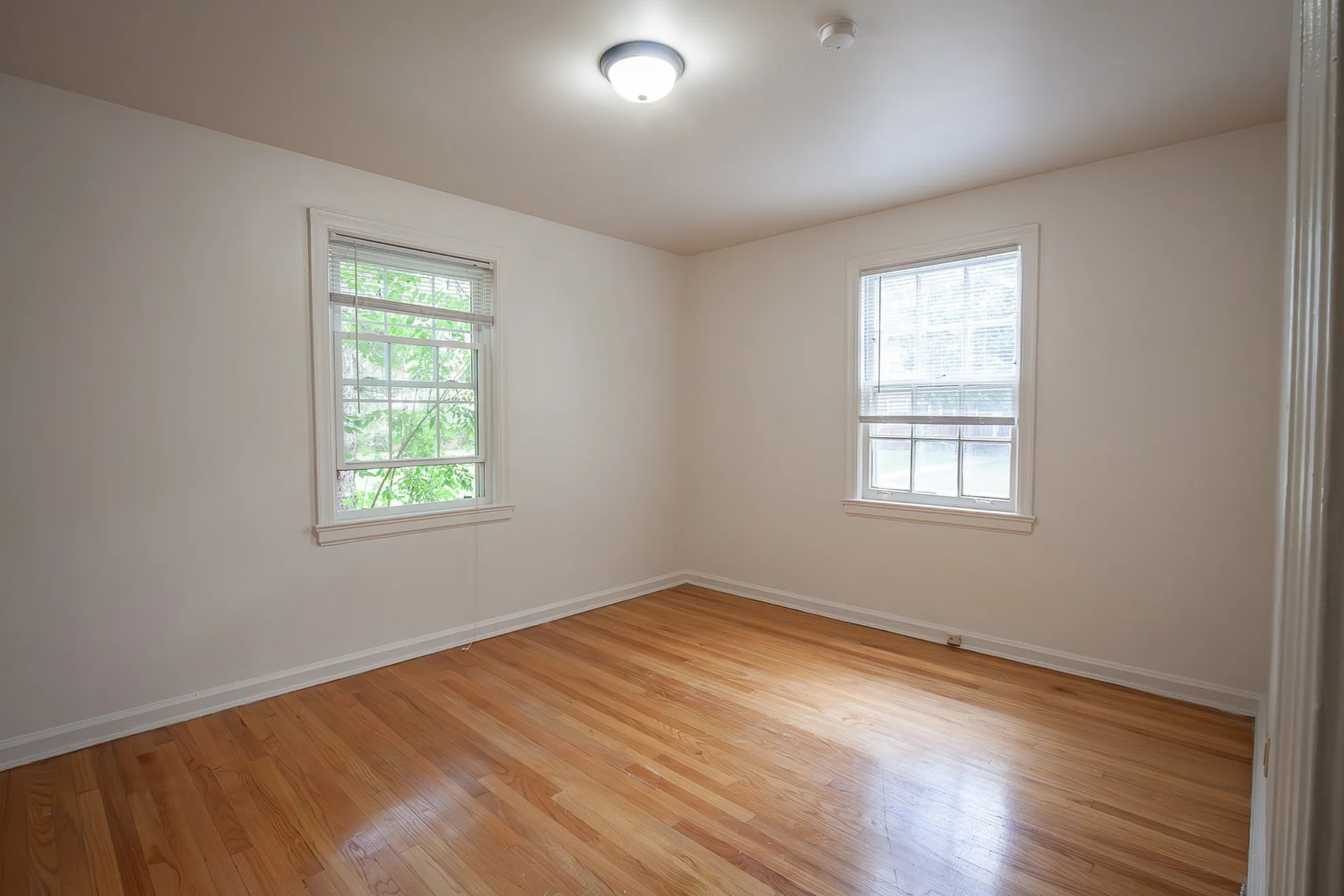 Bright and airy empty room featuring polished hardwood floors and large windows with abundant natural light.