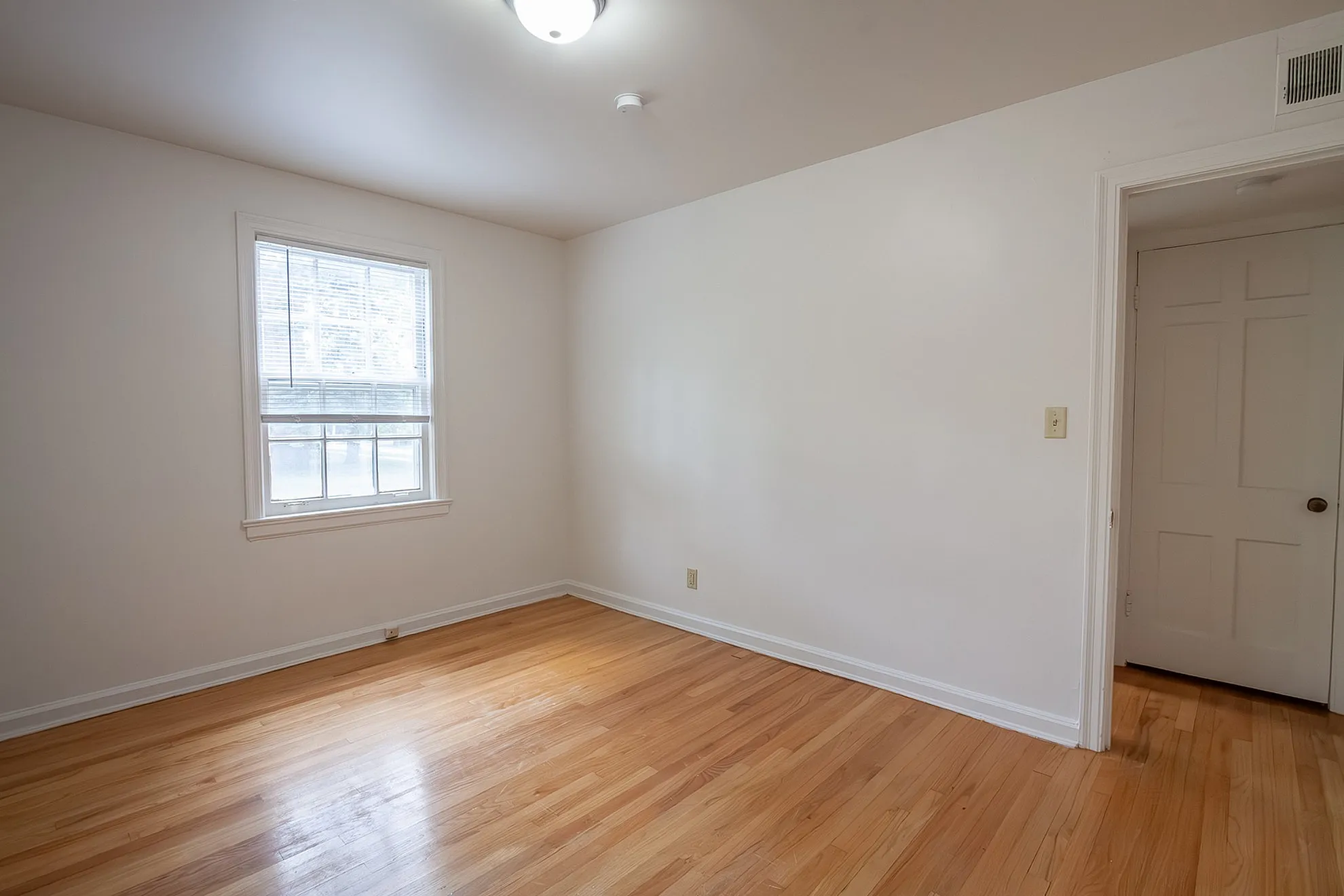 Bright and airy bedroom with polished hardwood floors and a large window offering natural light.