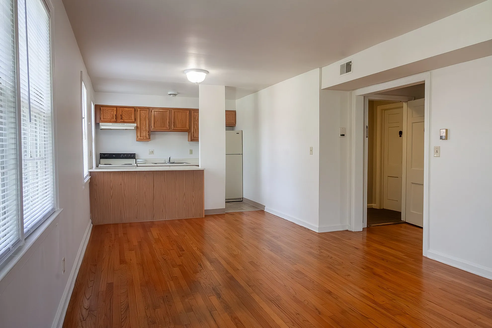Inviting open-concept living room featuring gleaming hardwood floors and a cozy kitchen with wooden cabinets.