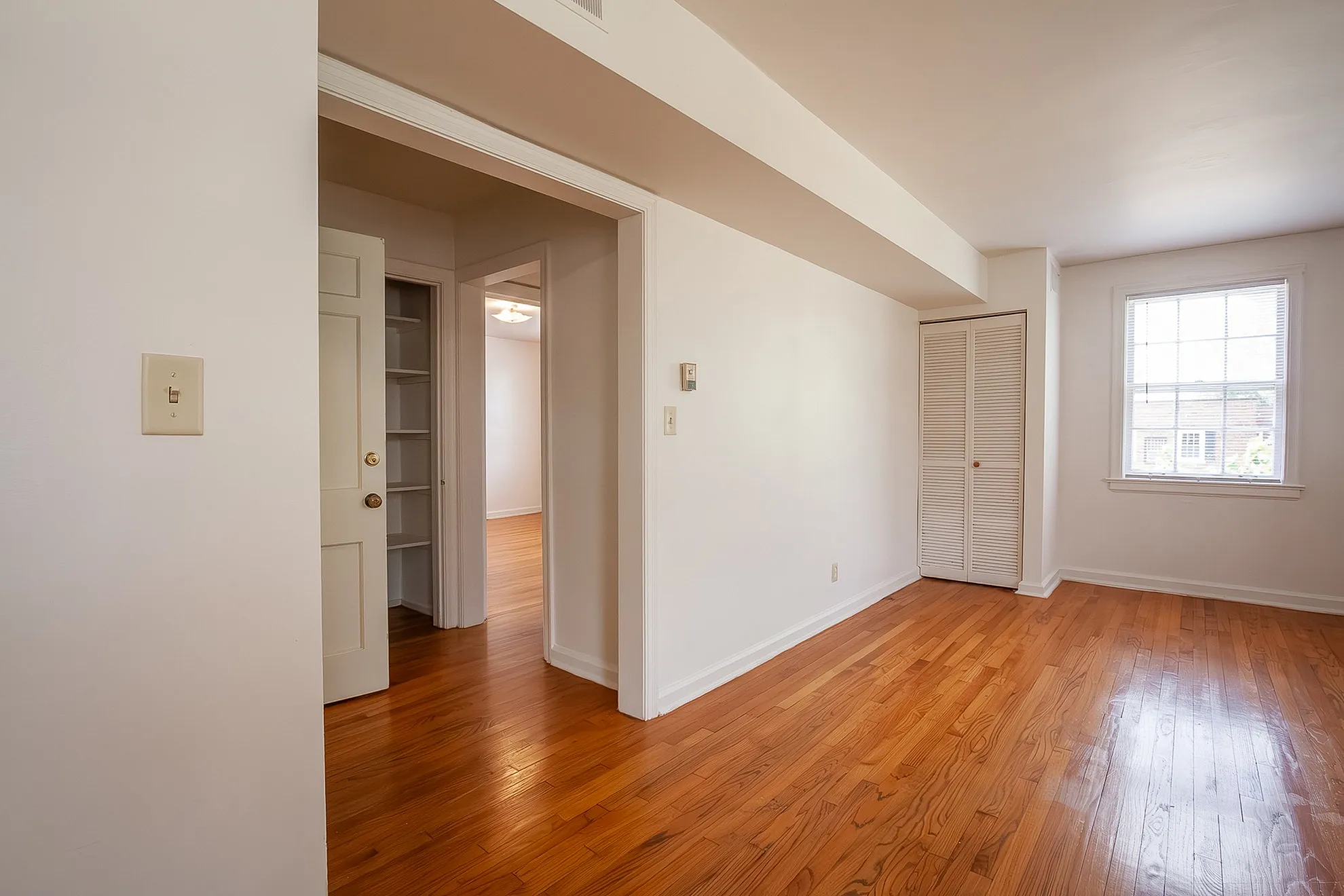 Bright and inviting apartment interior with hardwood floors, ample natural light from large windows, and convenient built-in shelving.