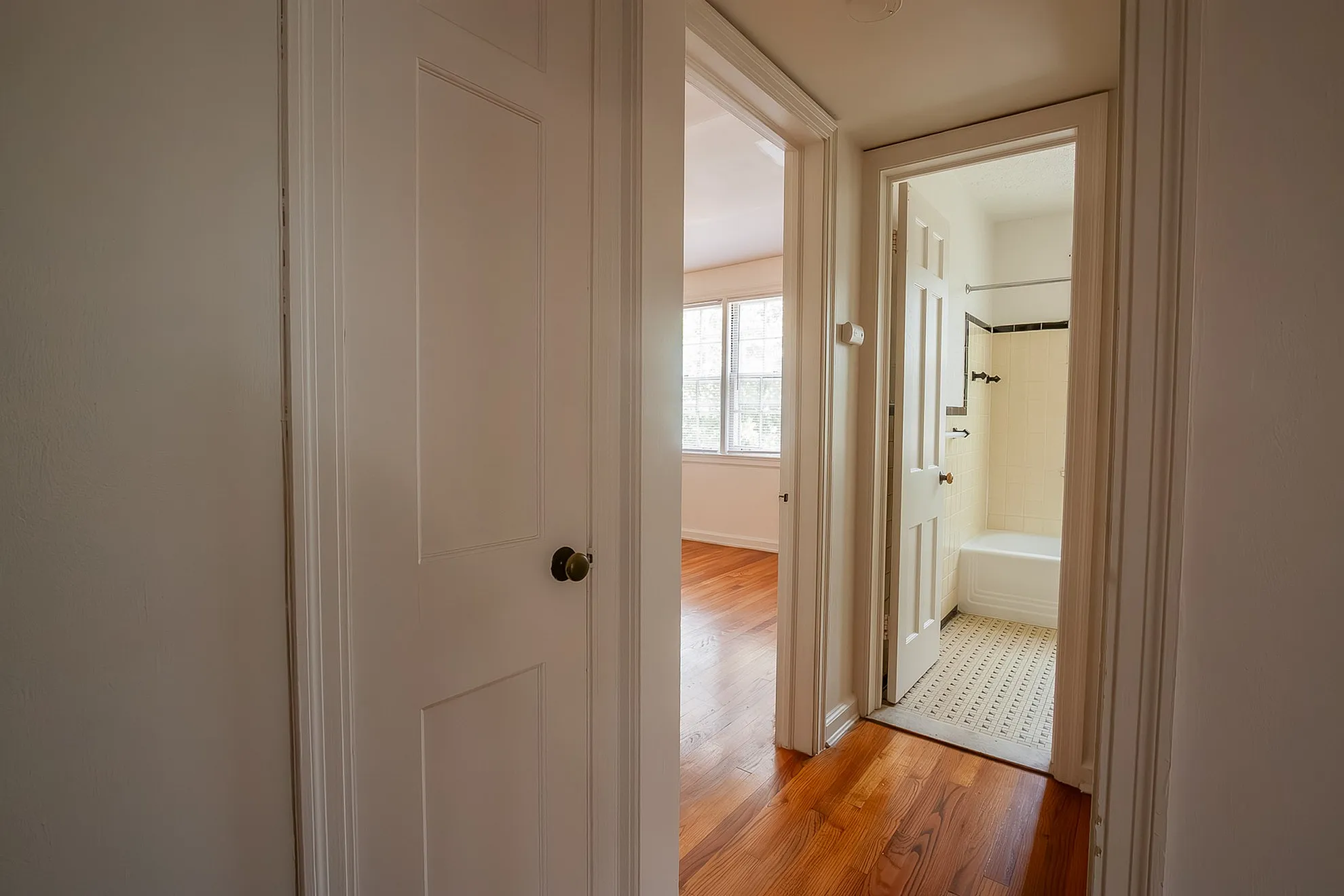 Inviting hallway leading to a sunlit bedroom and a modern bathroom with elegant wood flooring.